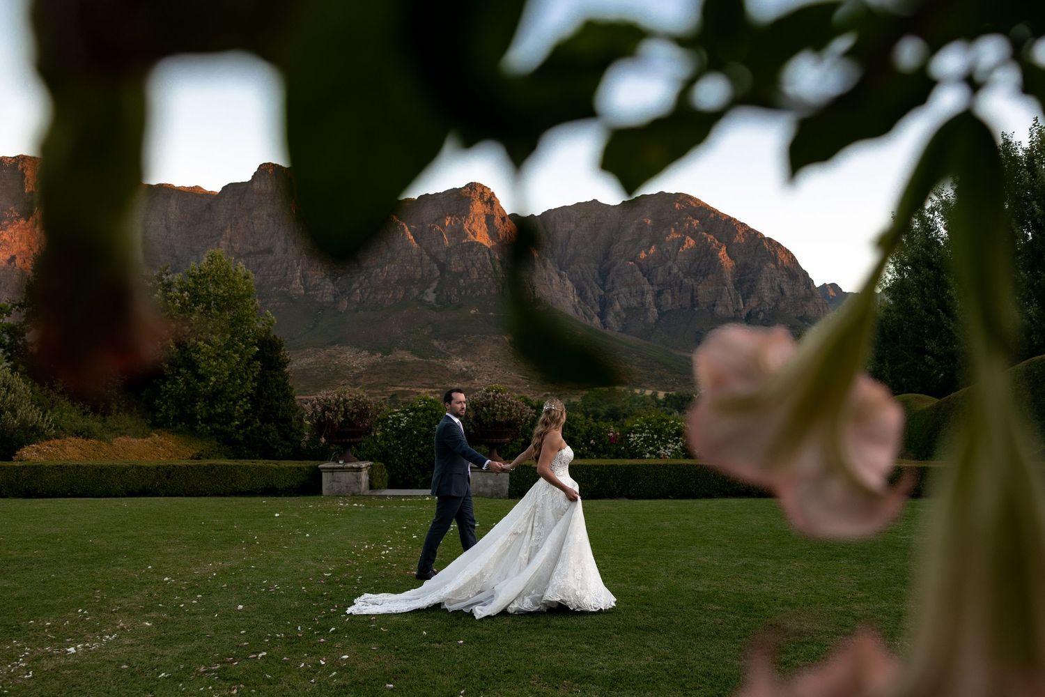 A couple dances on a lawn against a backdrop of majestic mountains glowing in sunset light.