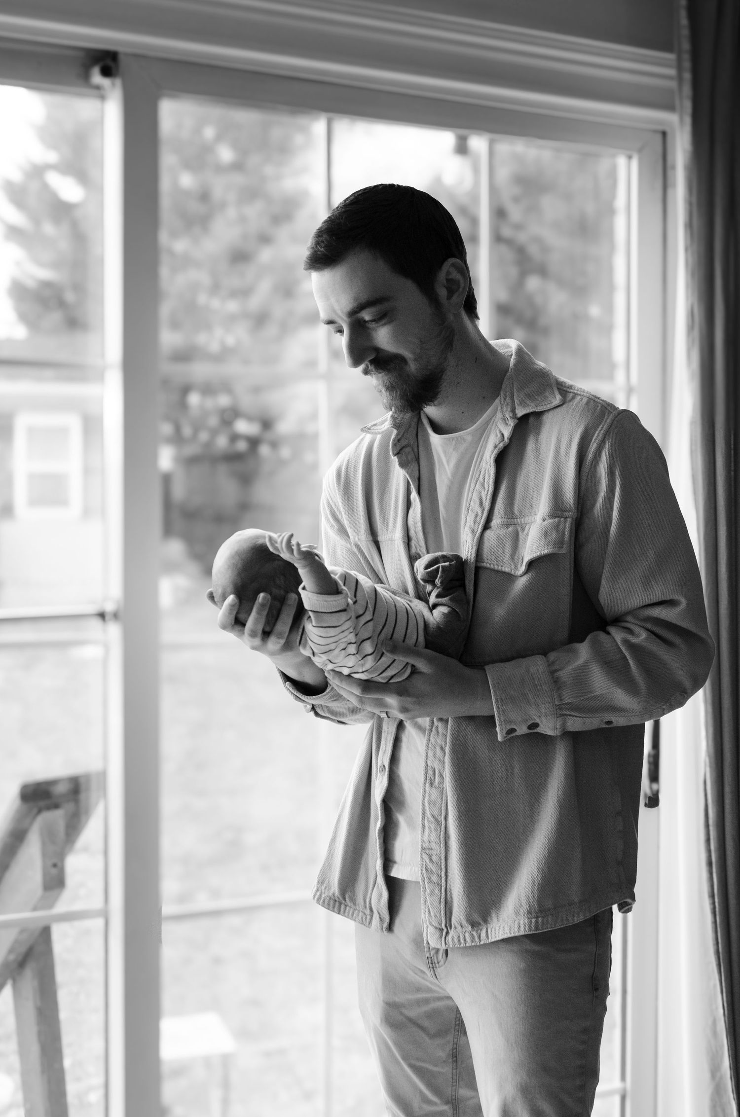 Silhouetted parent holding a baby near a bright window during a lifestyle newborn photography session in Charlotte, NC.
