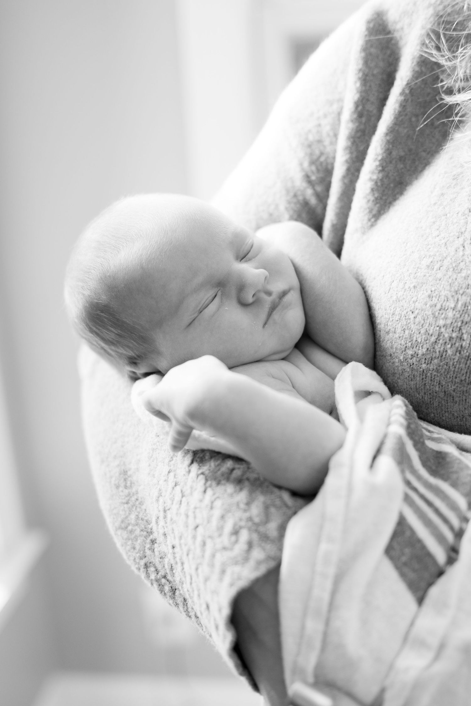 Black and white photo of a peacefully sleeping newborn baby cradled in an adult's arms, wrapped in a soft blanket.