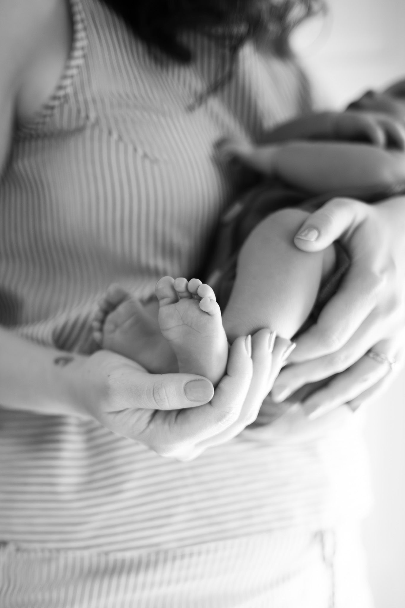 Black and white photo of a mother cradling her newborn baby, gently holding the infant's tiny feet in her hands.