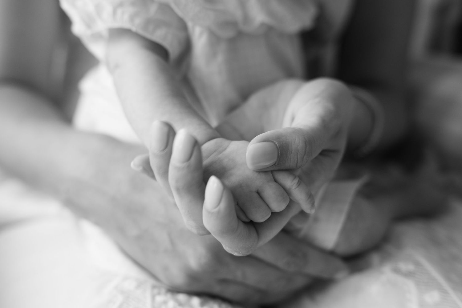 Black and white photo of an adult gently holding a small childs hands in a tender, loving gesture.