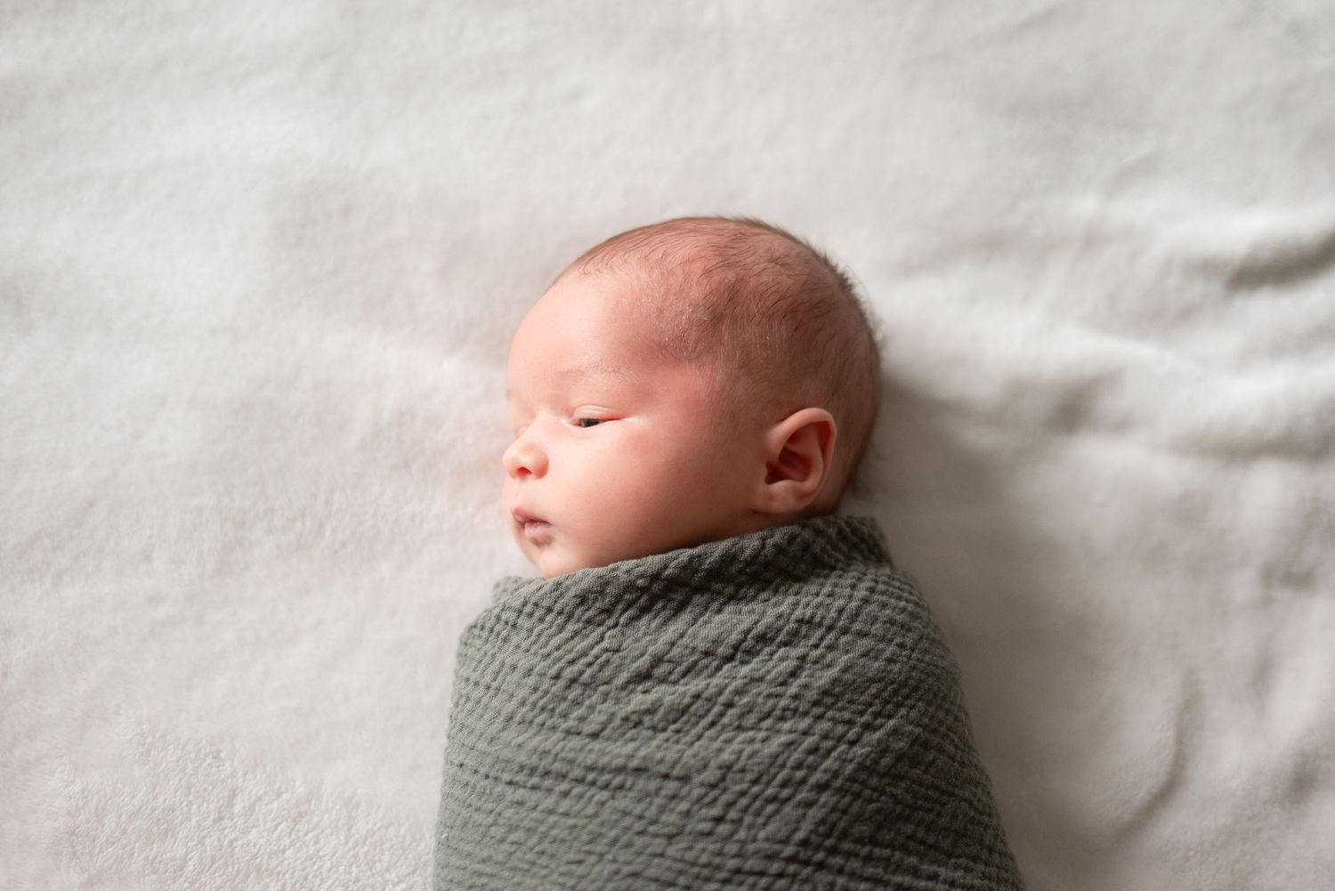 Peaceful newborn baby swaddled in a soft green wrap, sleeping on a white blanket.