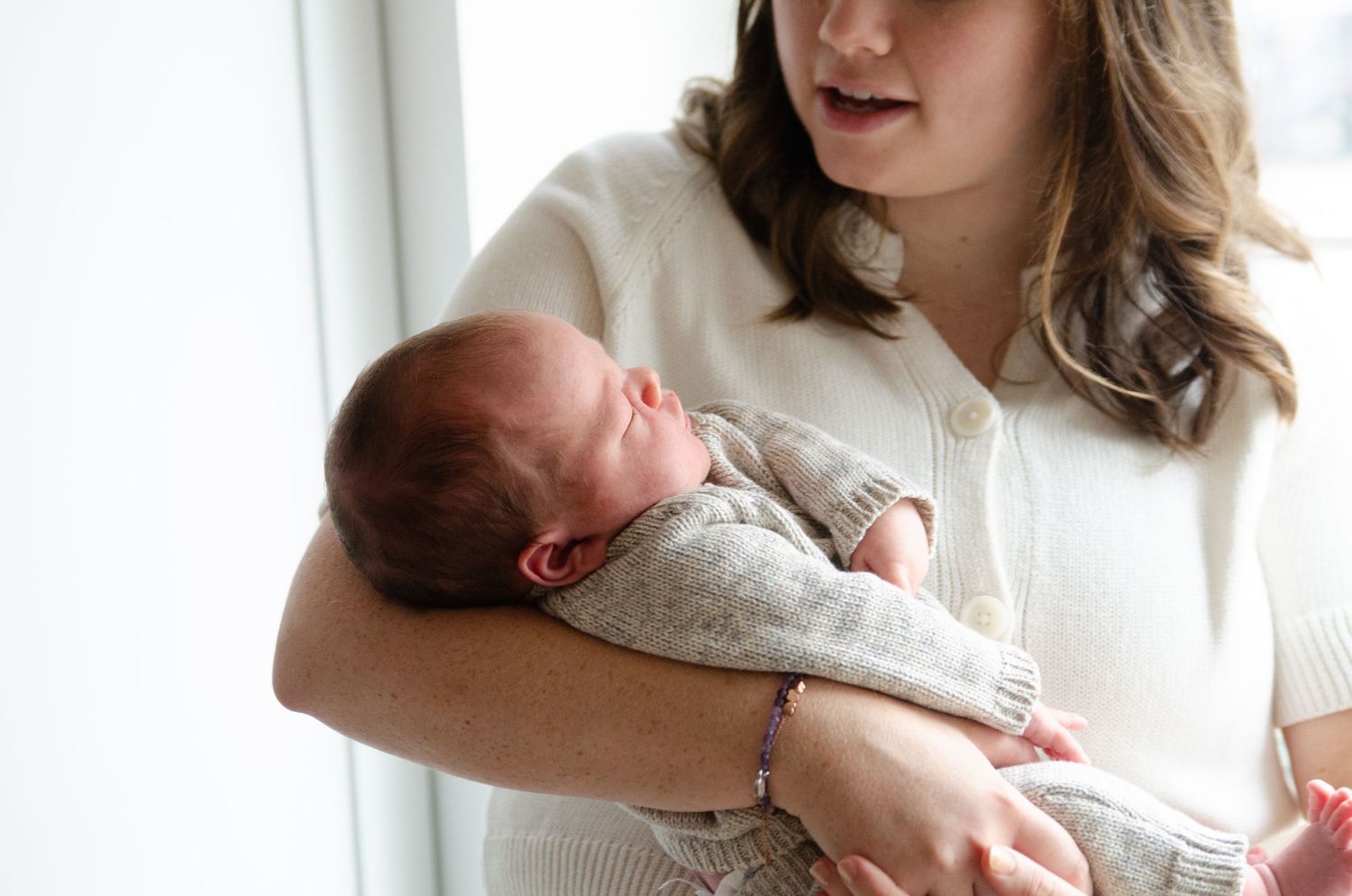 Parent holding a baby near a bright window during a lifestyle newborn photography session in Charlotte, NC.