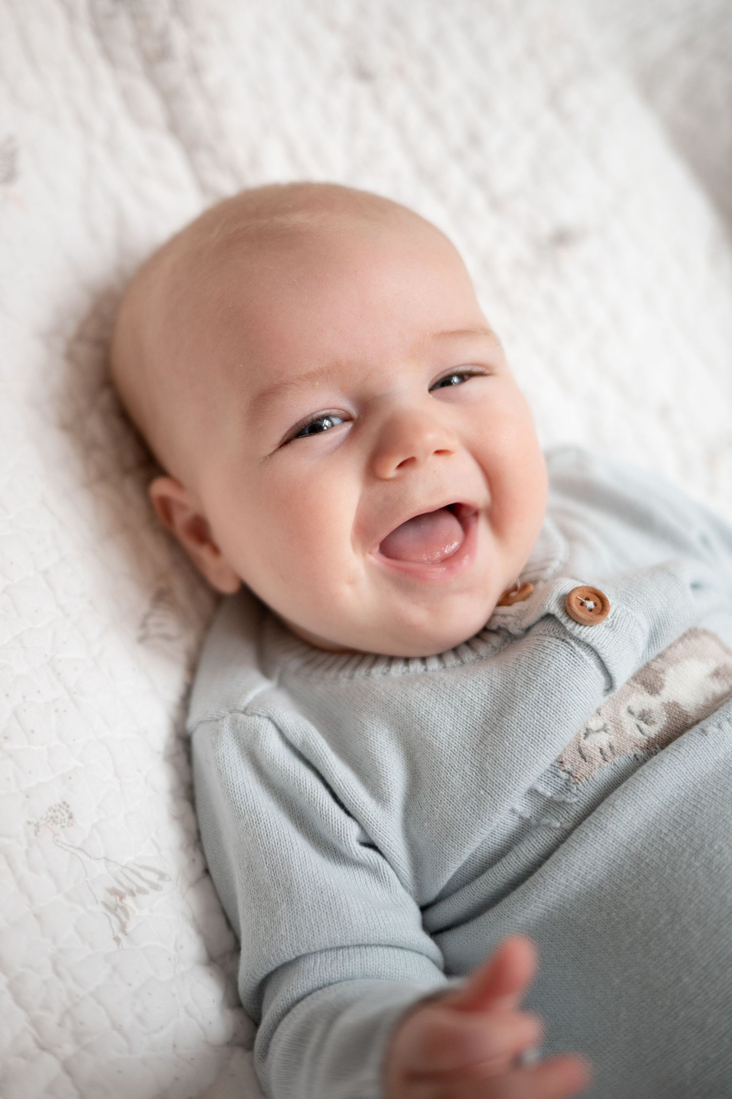 Happy baby laughing while lying on a white blanket during a lifestyle newborn photography session in Charlotte, NC.