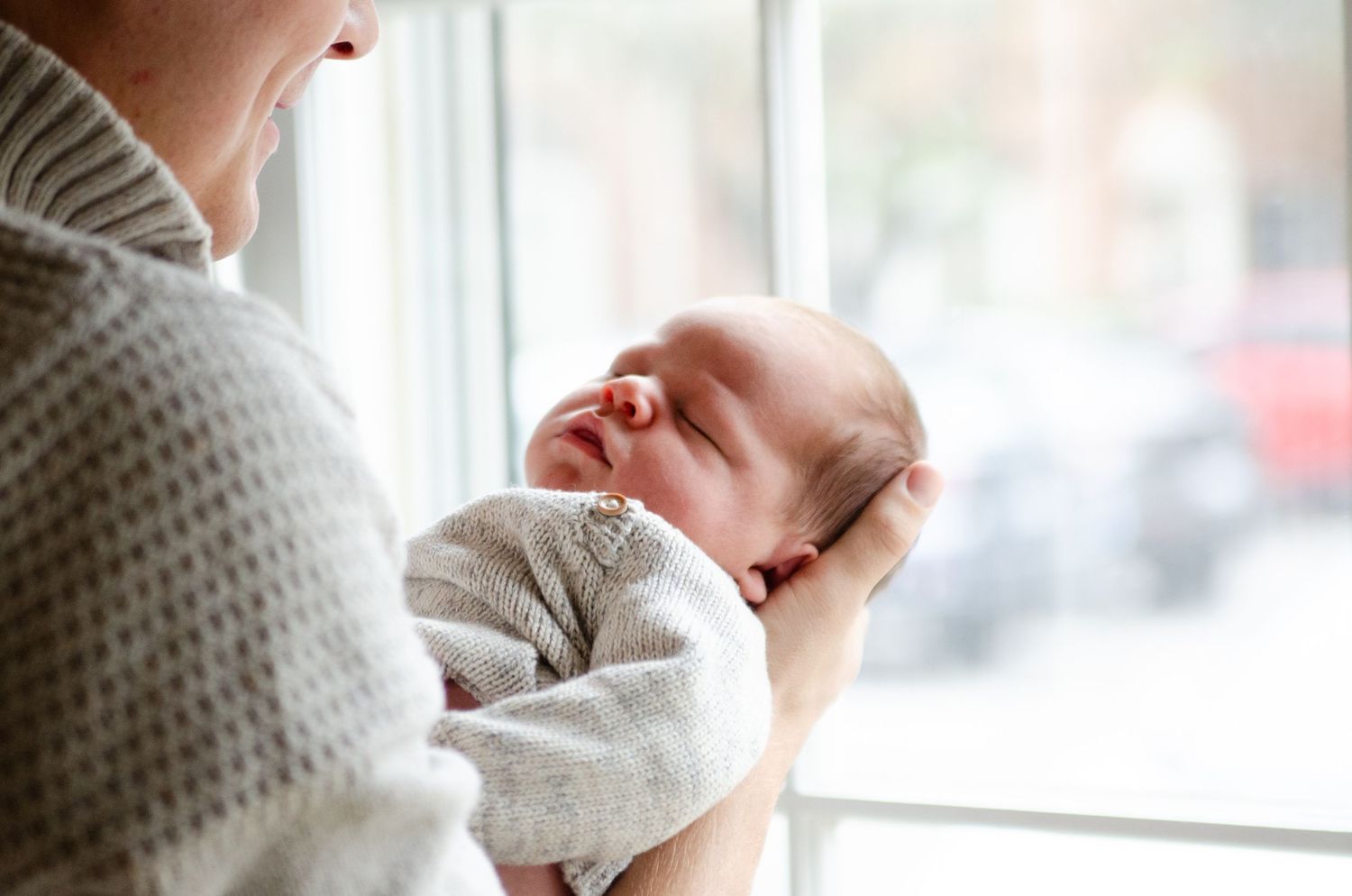 Parent holding their newborn by a bright window during a lifestyle in-home photo session in Charlotte, NC.