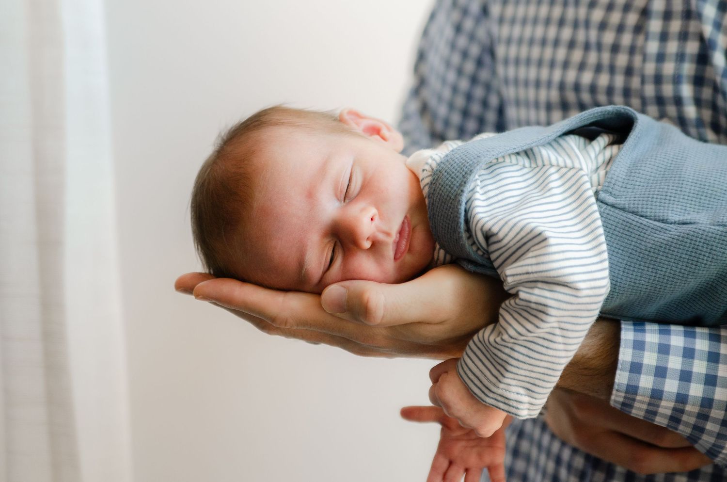 Sleeping baby resting in an adult’s palm by a window during a lifestyle newborn photography session in Charlotte, NC.