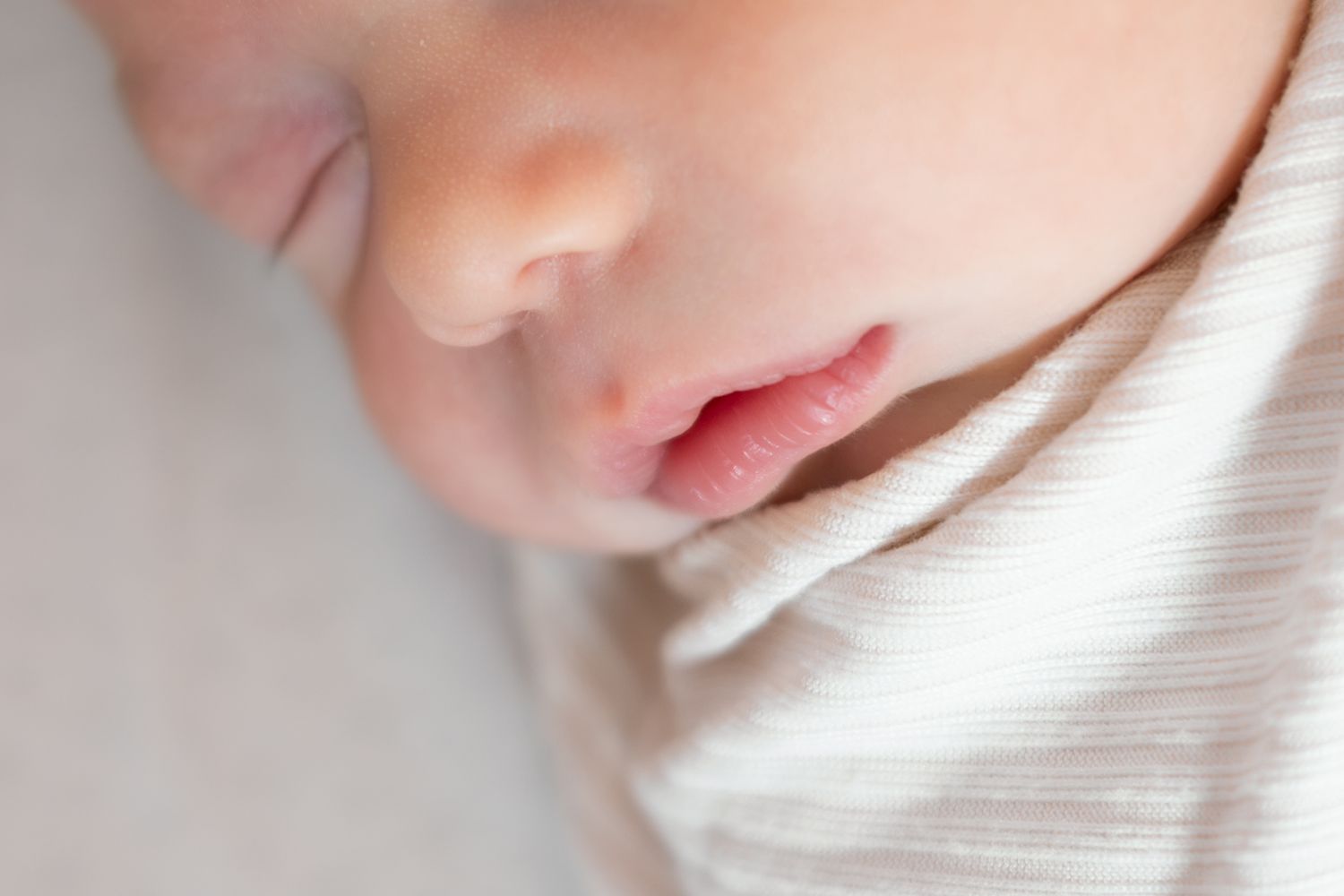 Close-up of a sleeping newborn baby's face with soft pink lips and delicate skin wrapped in a white swaddle.