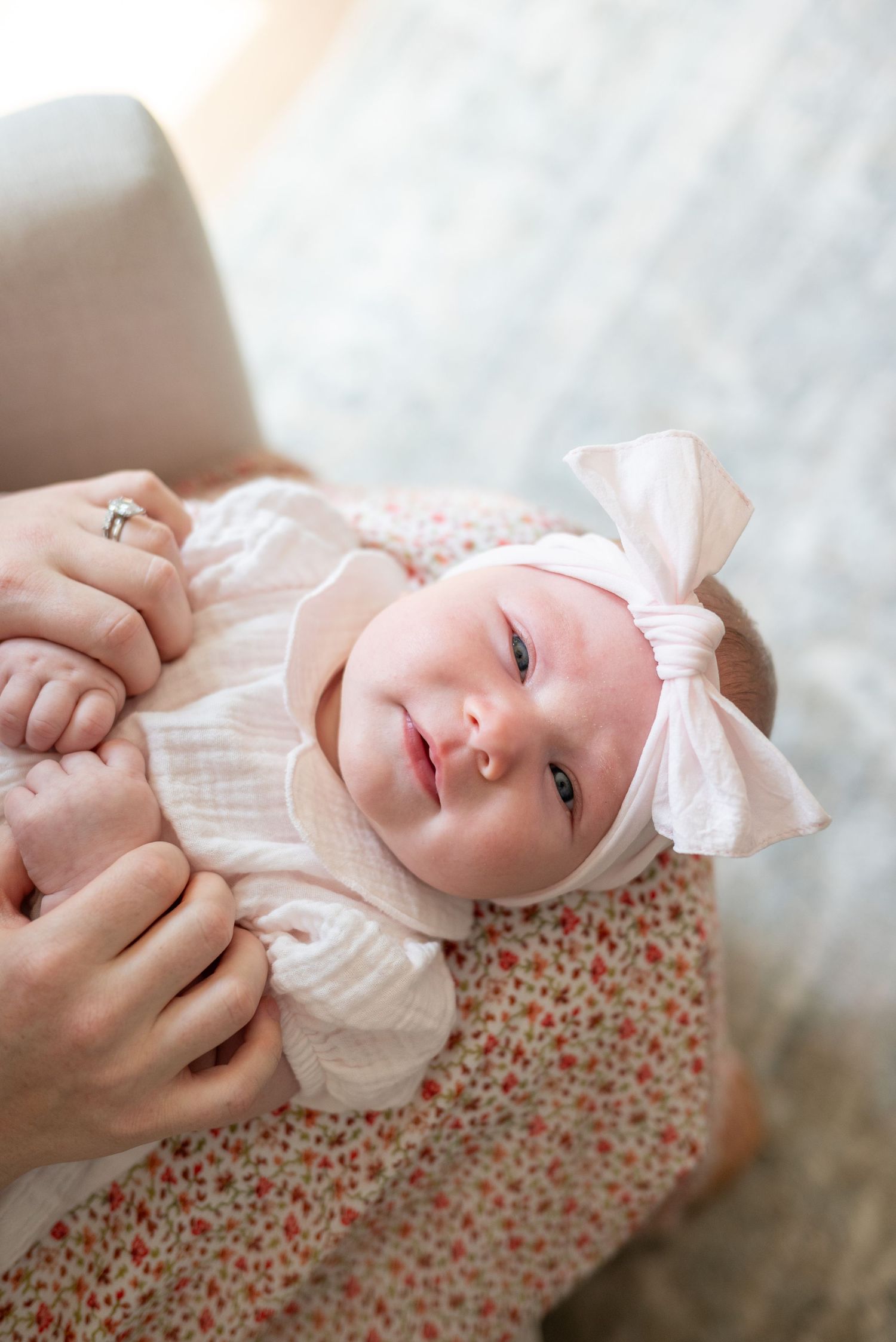A newborn baby girl in a white outfit and pink bow headband being cradled in a parent's arms.
