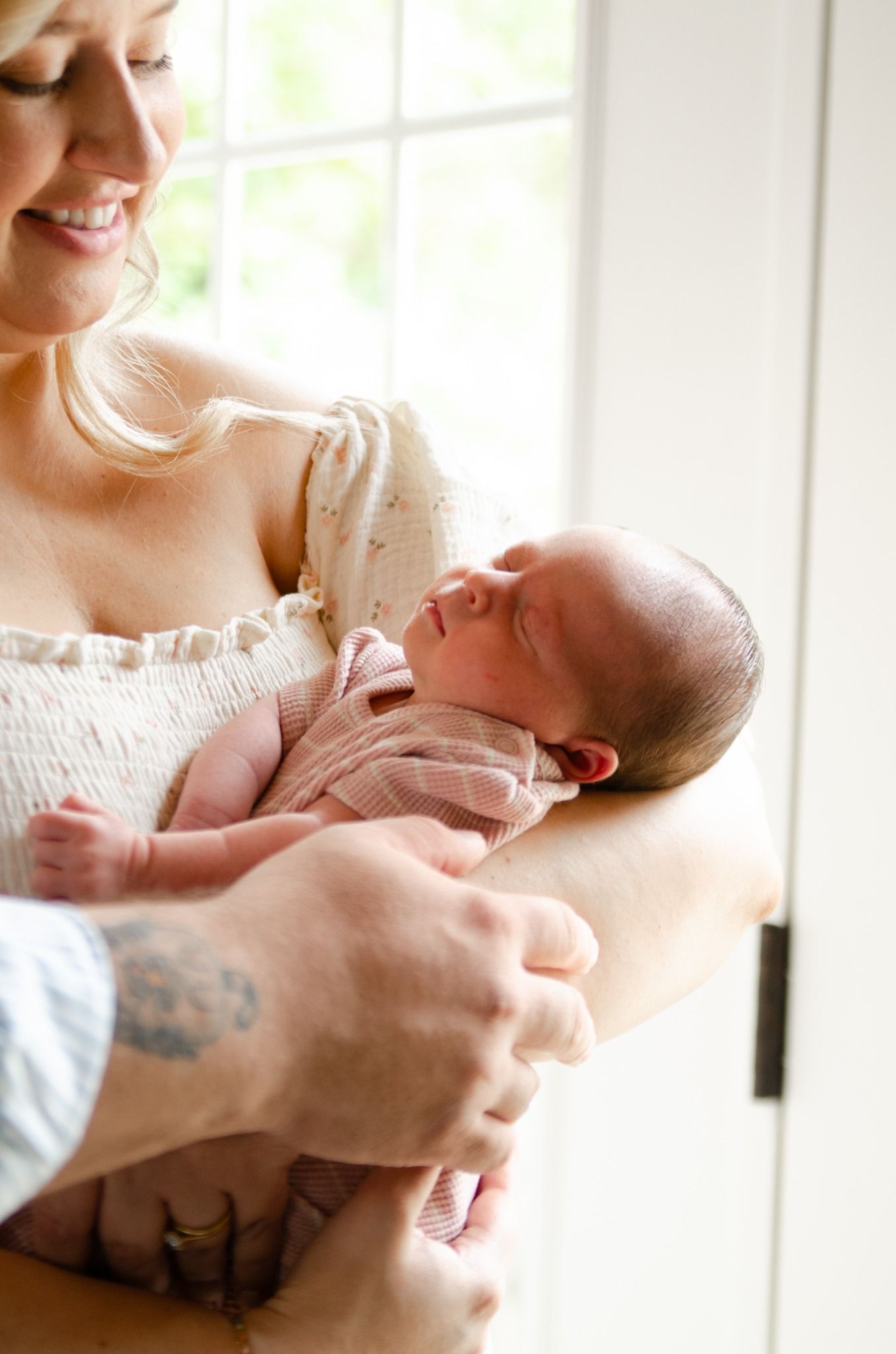 Parent cradling a sleeping newborn near a bright window during a lifestyle newborn photography session in Charlotte, NC.