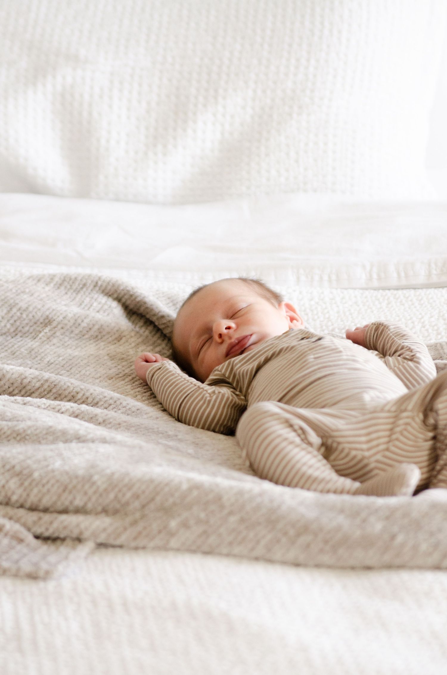 Peaceful newborn sleeping on white bedding during a lifestyle newborn photography session in Charlotte, NC.