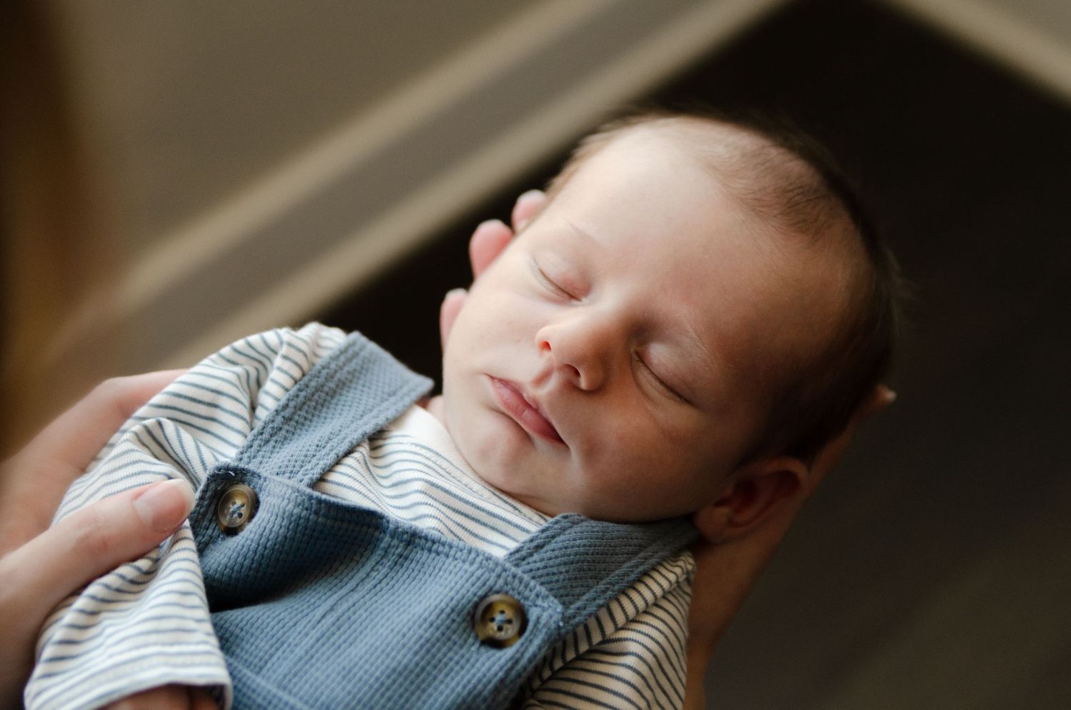 Sleeping newborn wearing blue overalls captured in soft natural light during a lifestyle newborn photography session in Charlotte, NC.