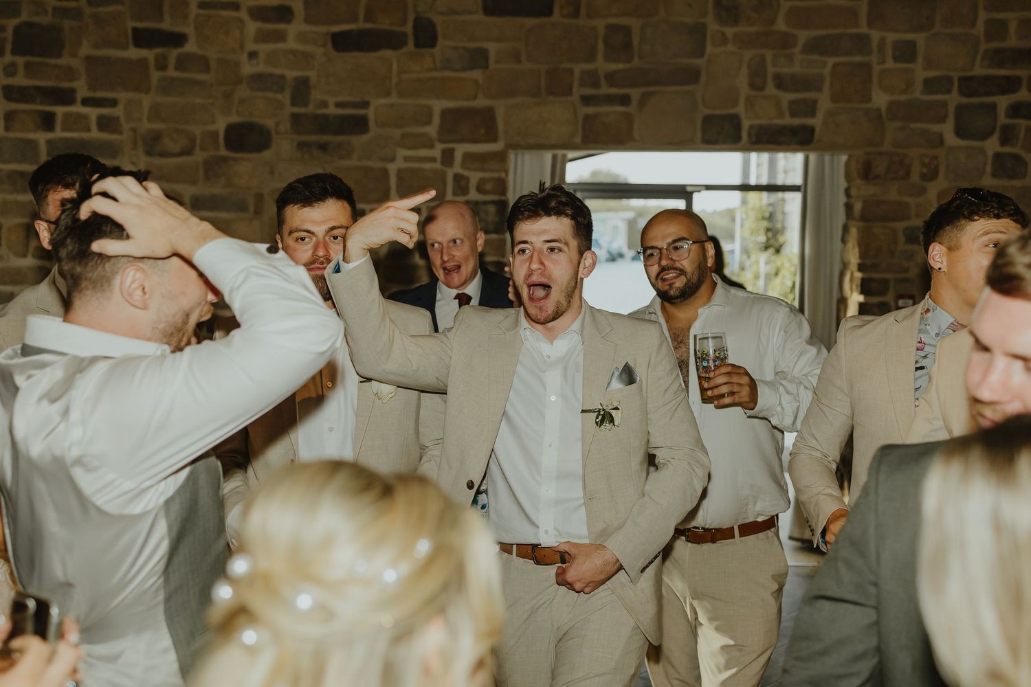 Groomsmen in light gray suits dancing and celebrating at a wedding reception.