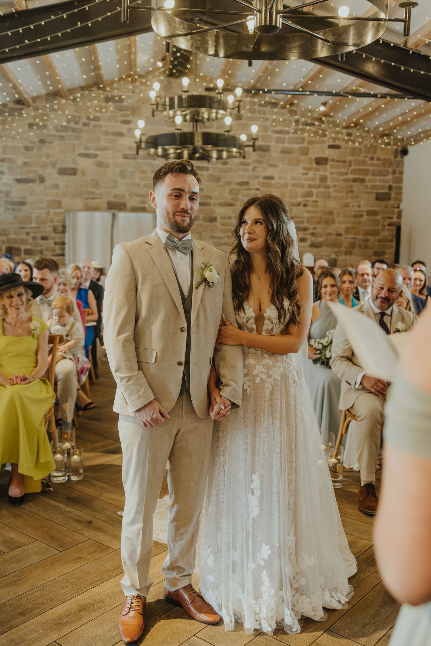 Newlyweds walking down the aisle in a rustic venue with string lights and exposed brick walls.
