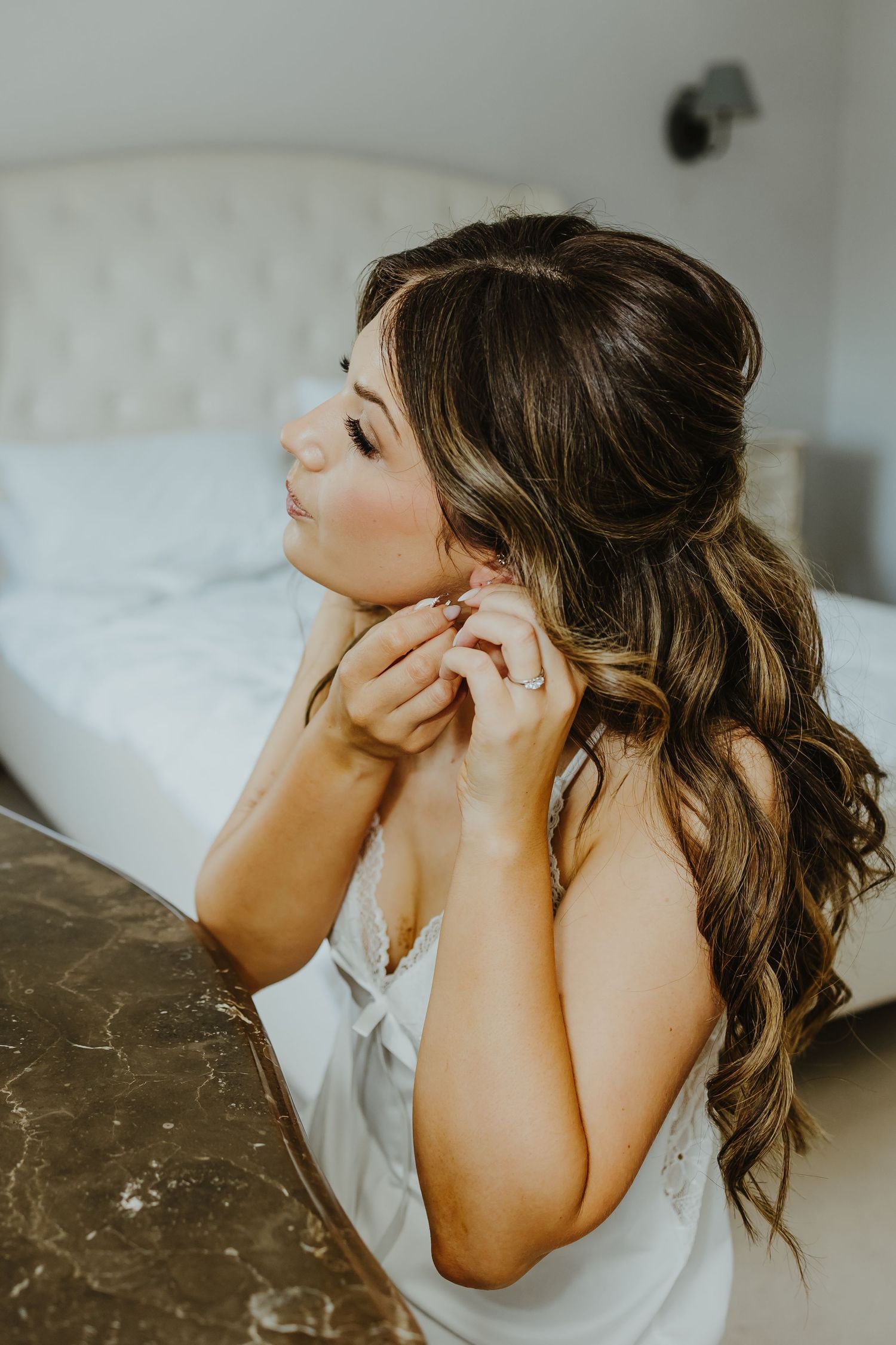 Close-up of someone putting on delicate jewelry while wearing a white top.