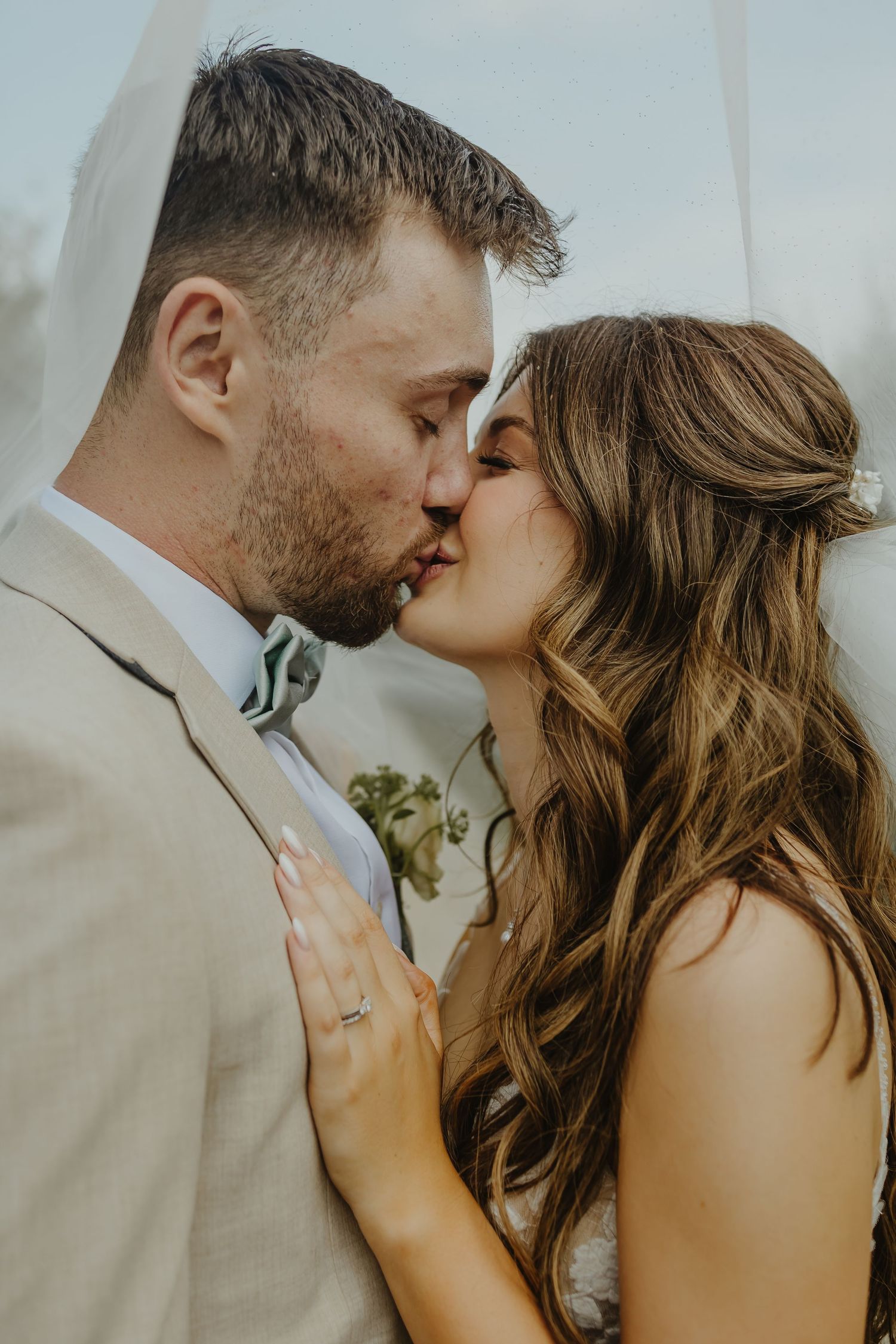 Newlyweds embrace in a tender moment with sunlight filtering through a delicate veil.