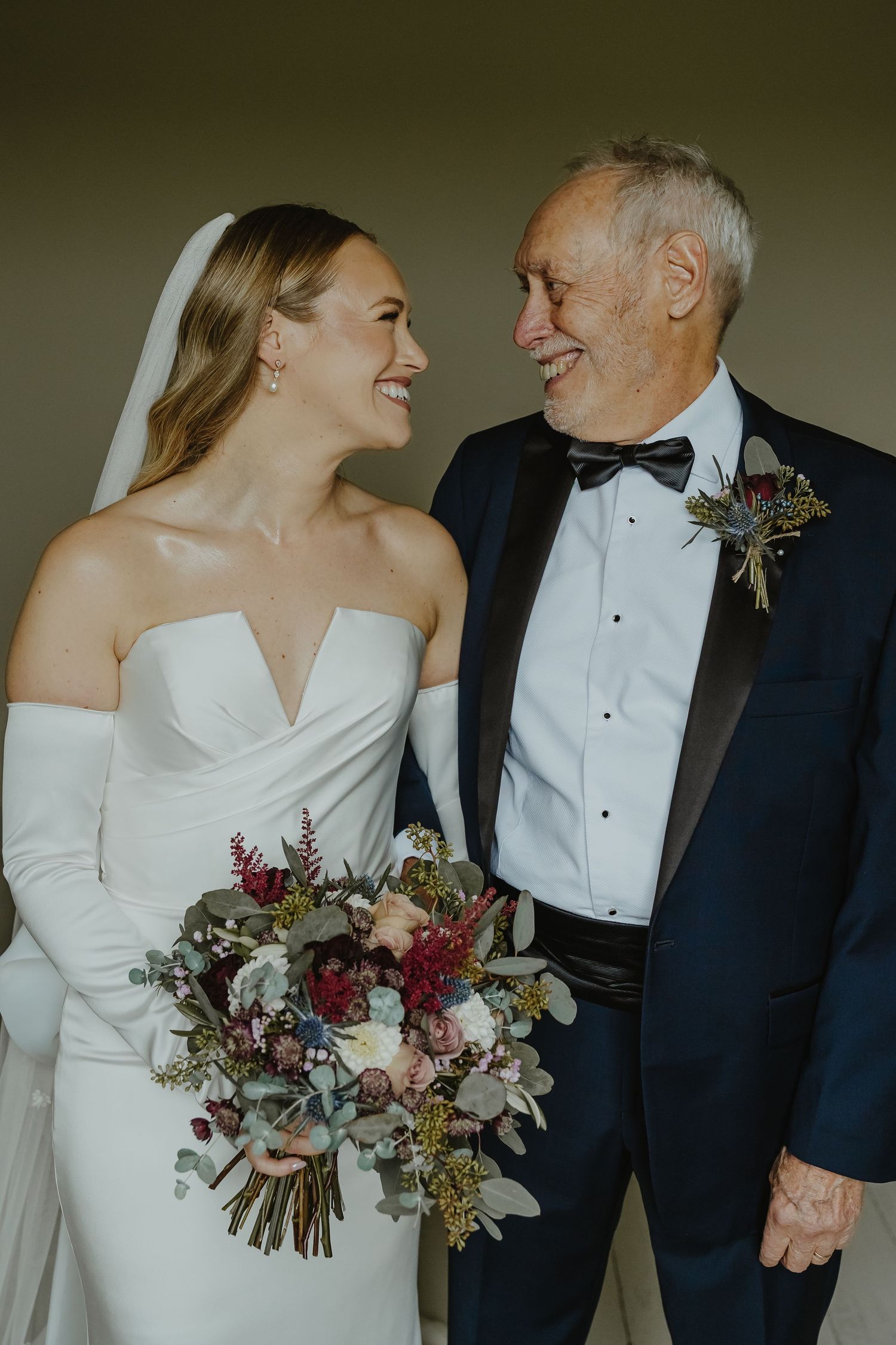 Elegant couple shares joyful moments in formal wedding attire with a stunning burgundy and eucalyptus bouquet.