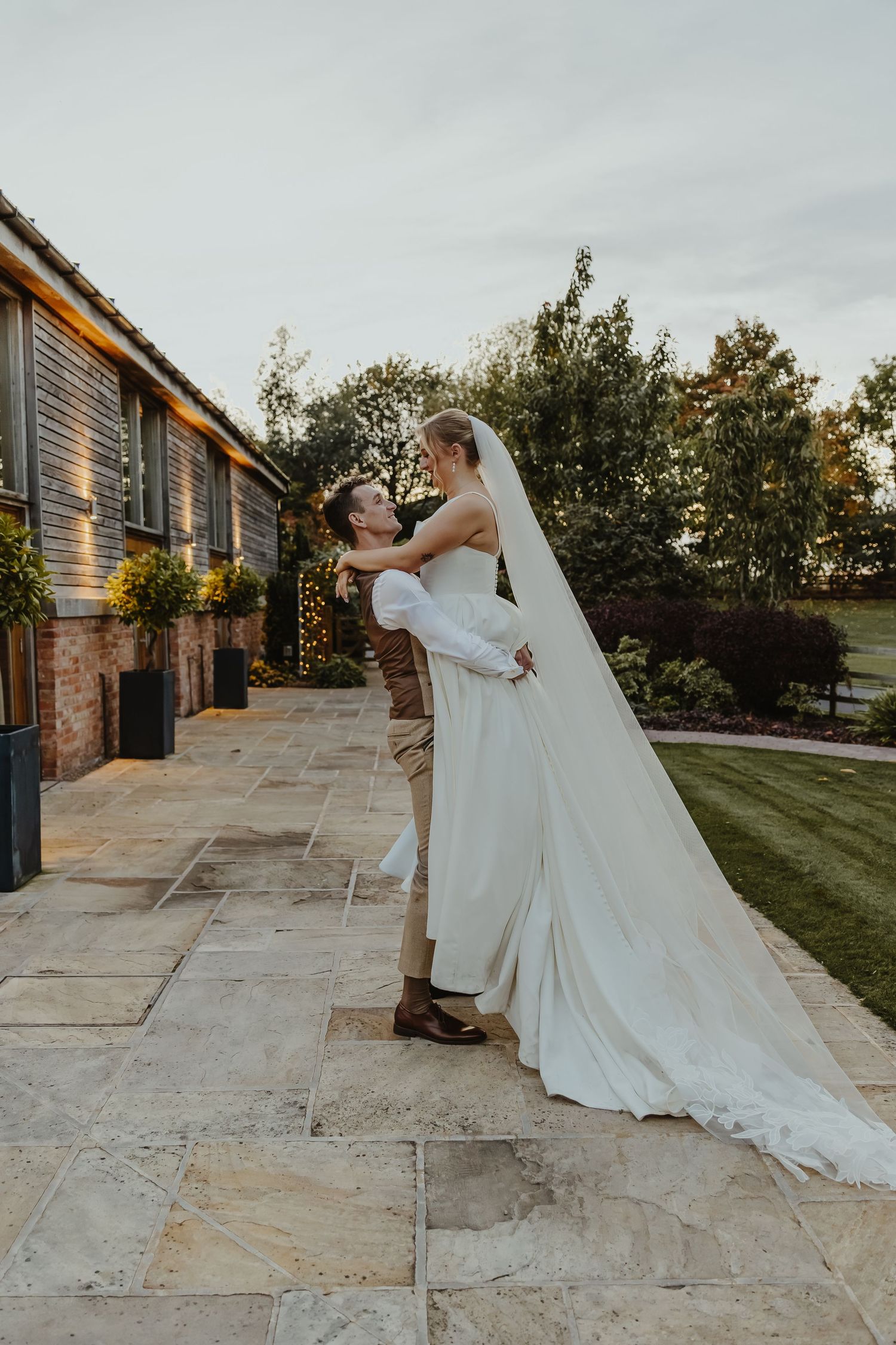 Wedding couple dances and twirls on stone patio during sunset celebration.