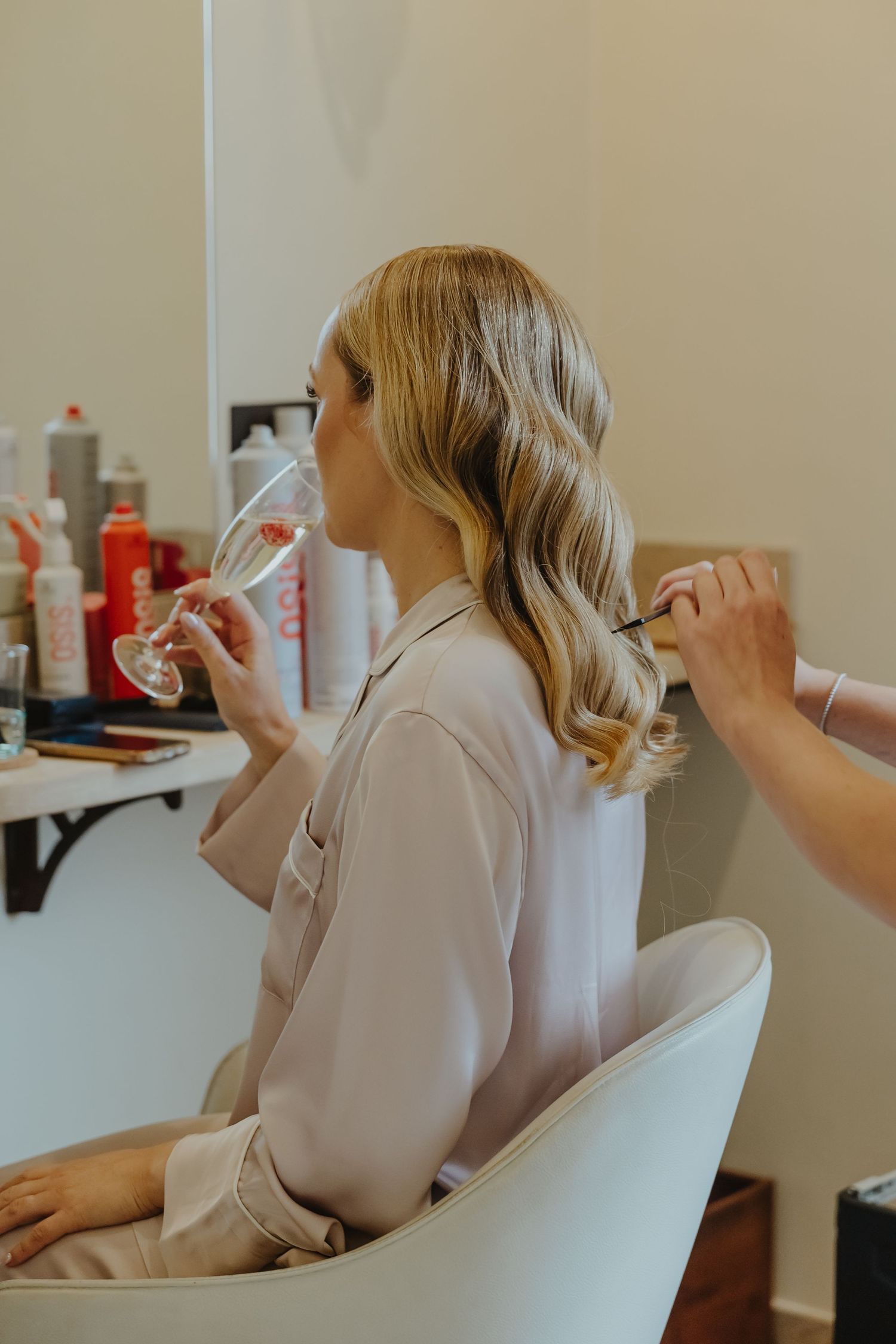 Wedding day preparation scene showing hair styling in progress in a bright room.