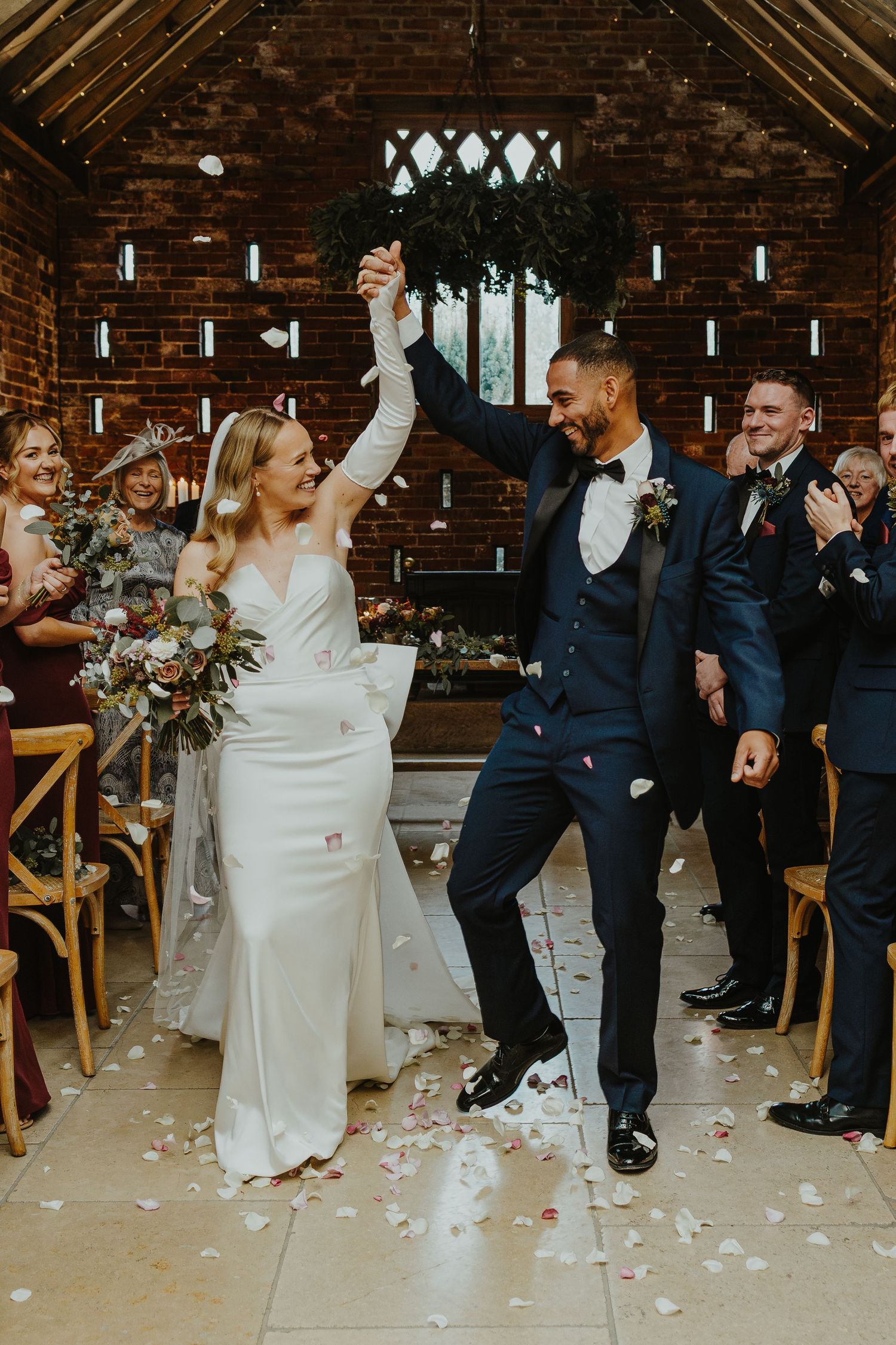 Wedding couple and guests dancing through shower of white confetti in rustic venue.