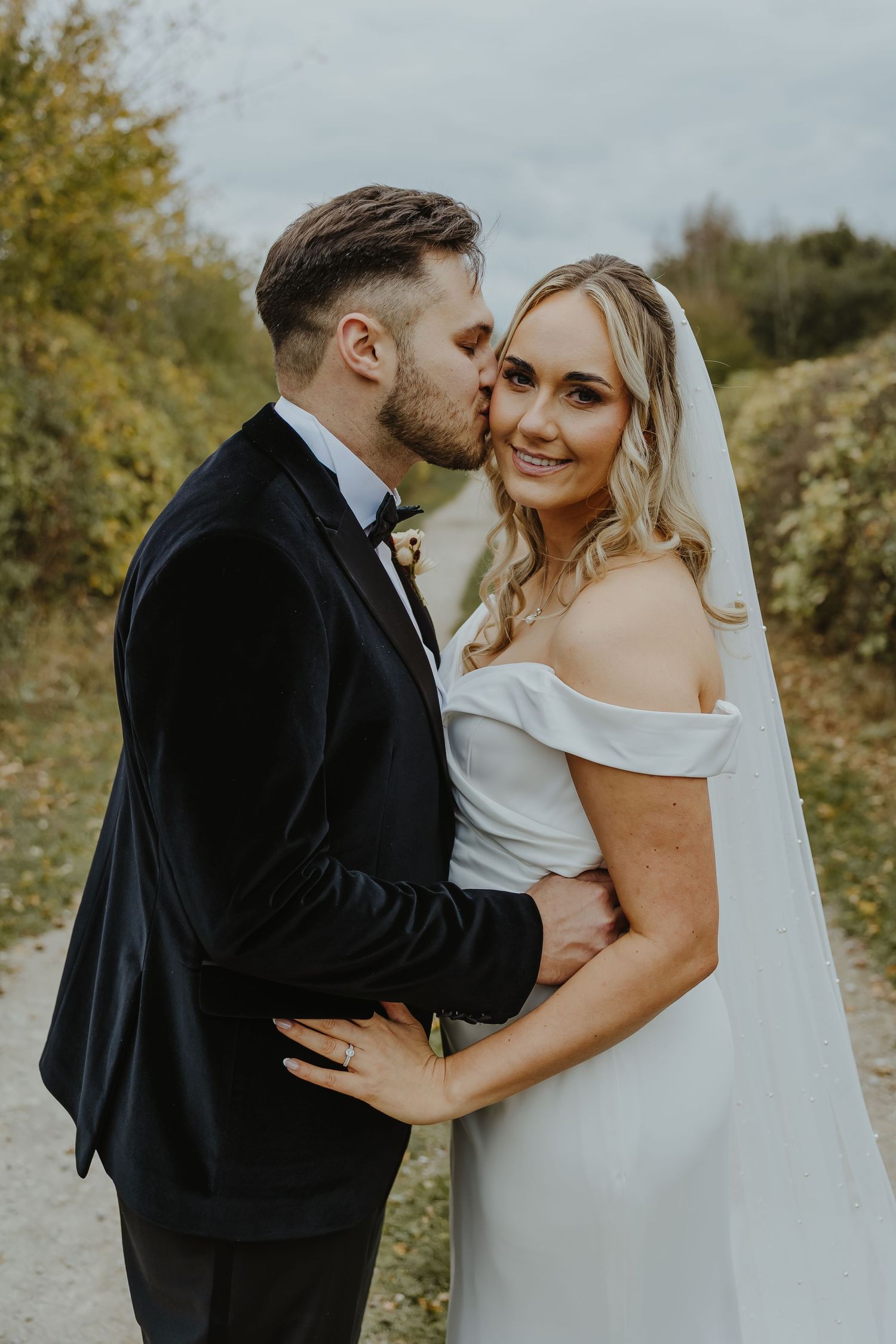 Intimate wedding couple moment captured on a nature path in formal attire.