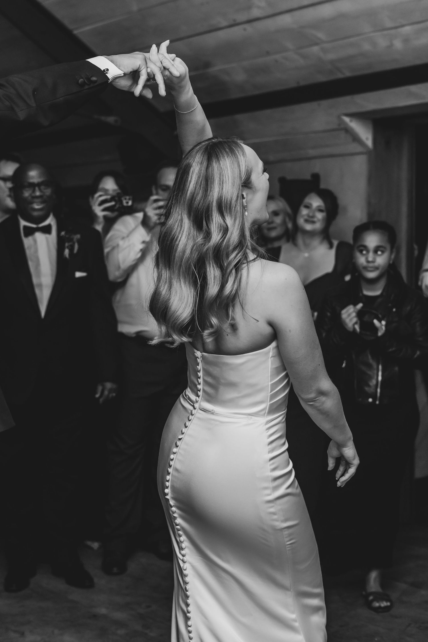 A bride in a fitted white dress dances at her wedding reception while guests watch and smile in the background.
