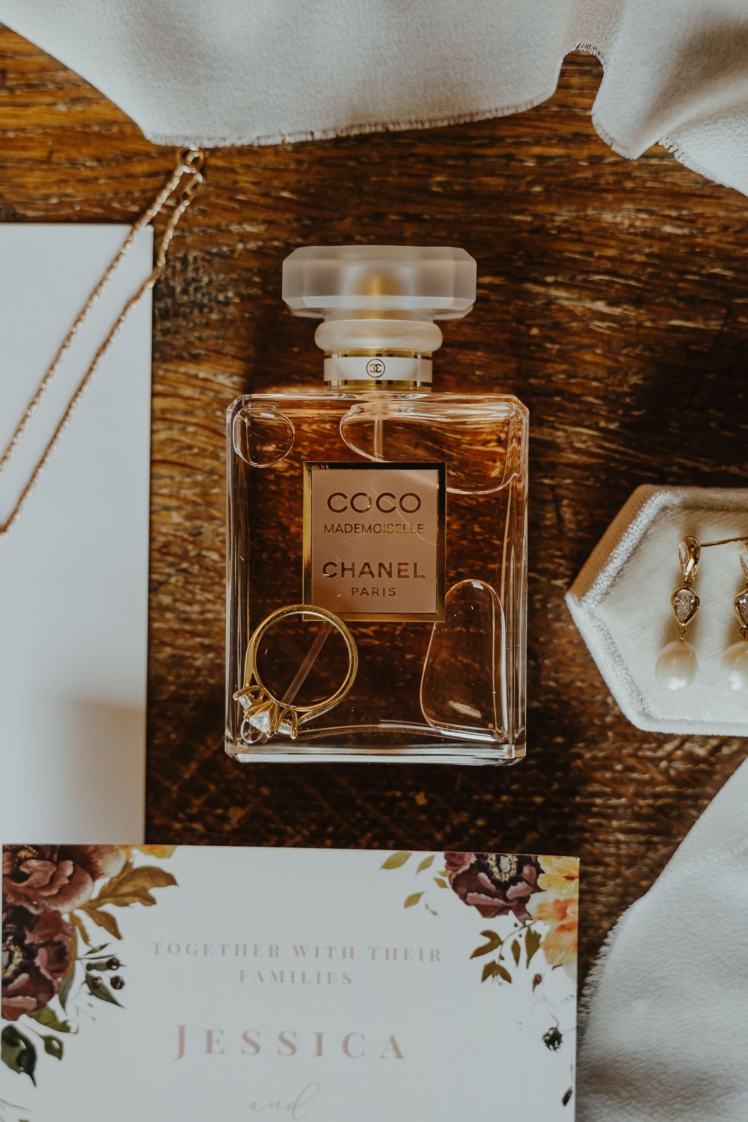 Luxury perfume bottles and wedding stationery with floral designs displayed on dark wooden surface.