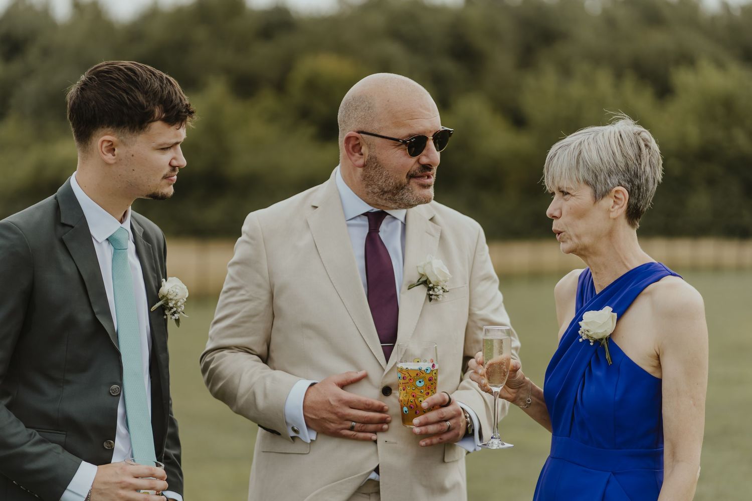Wedding guests enjoy drinks and conversation on a sunny outdoor lawn during a celebration.