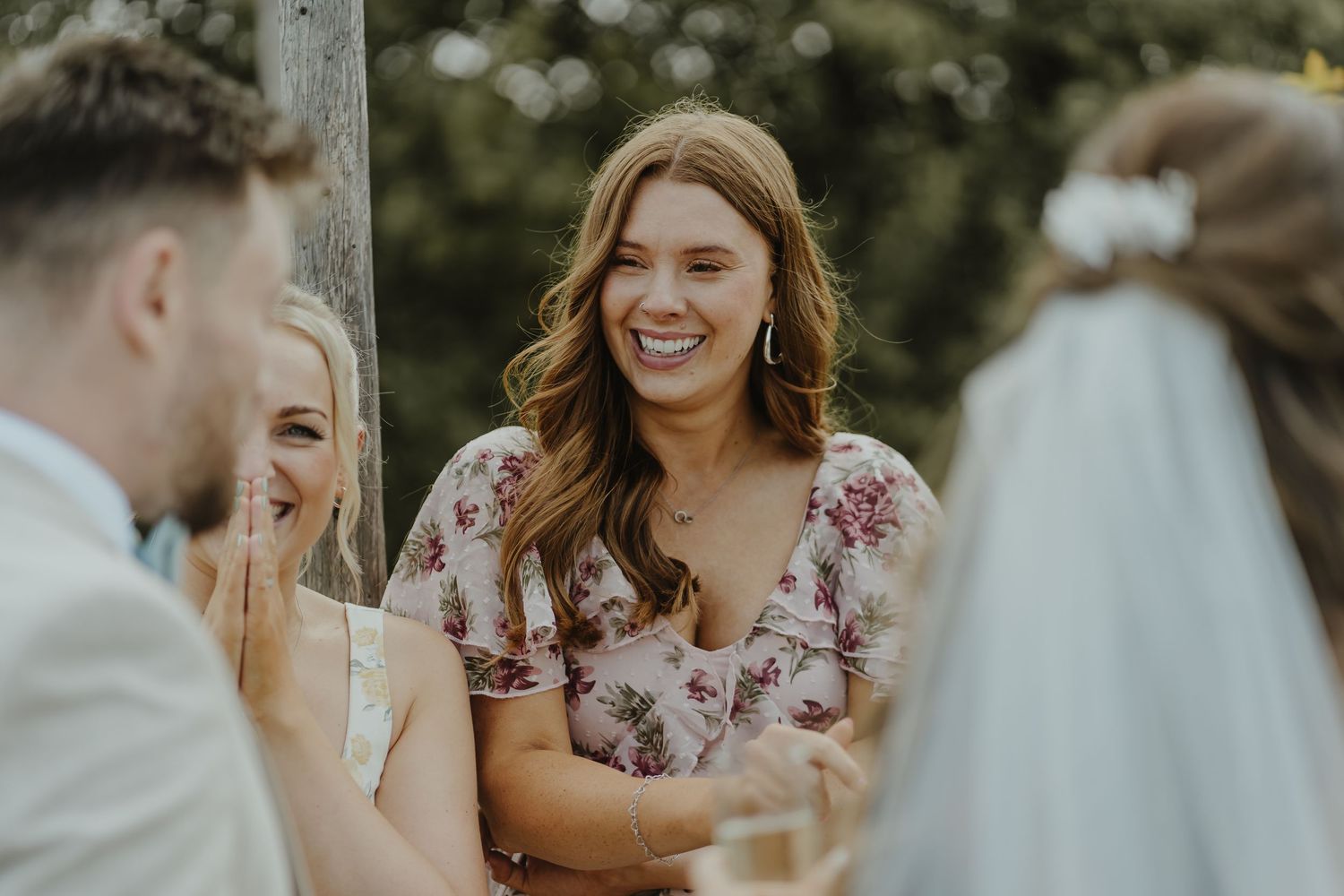 A joyful moment shared between wedding guests in floral dresses during an outdoor celebration.