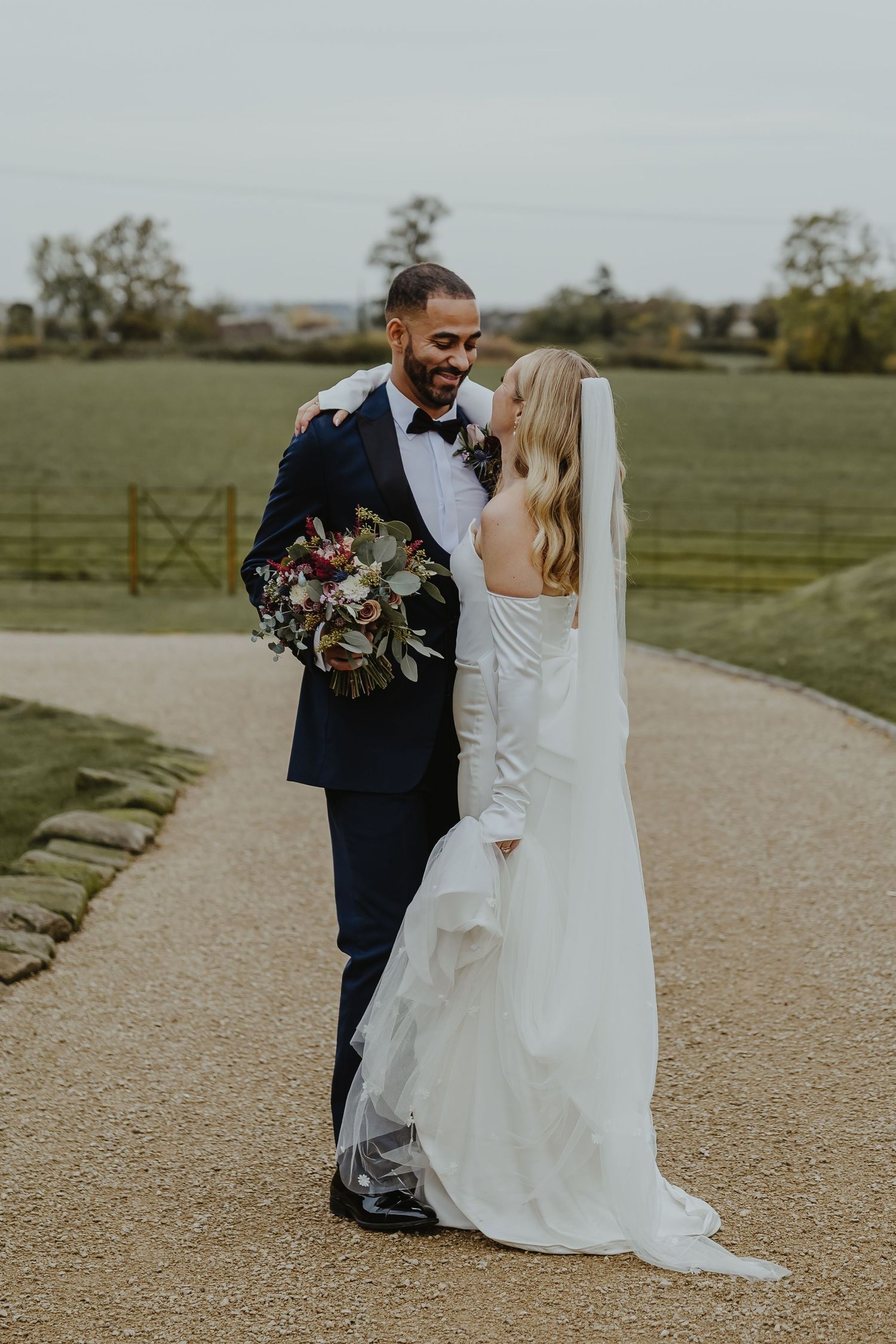 Newlyweds sharing intimate moment on stone path with countryside backdrop.