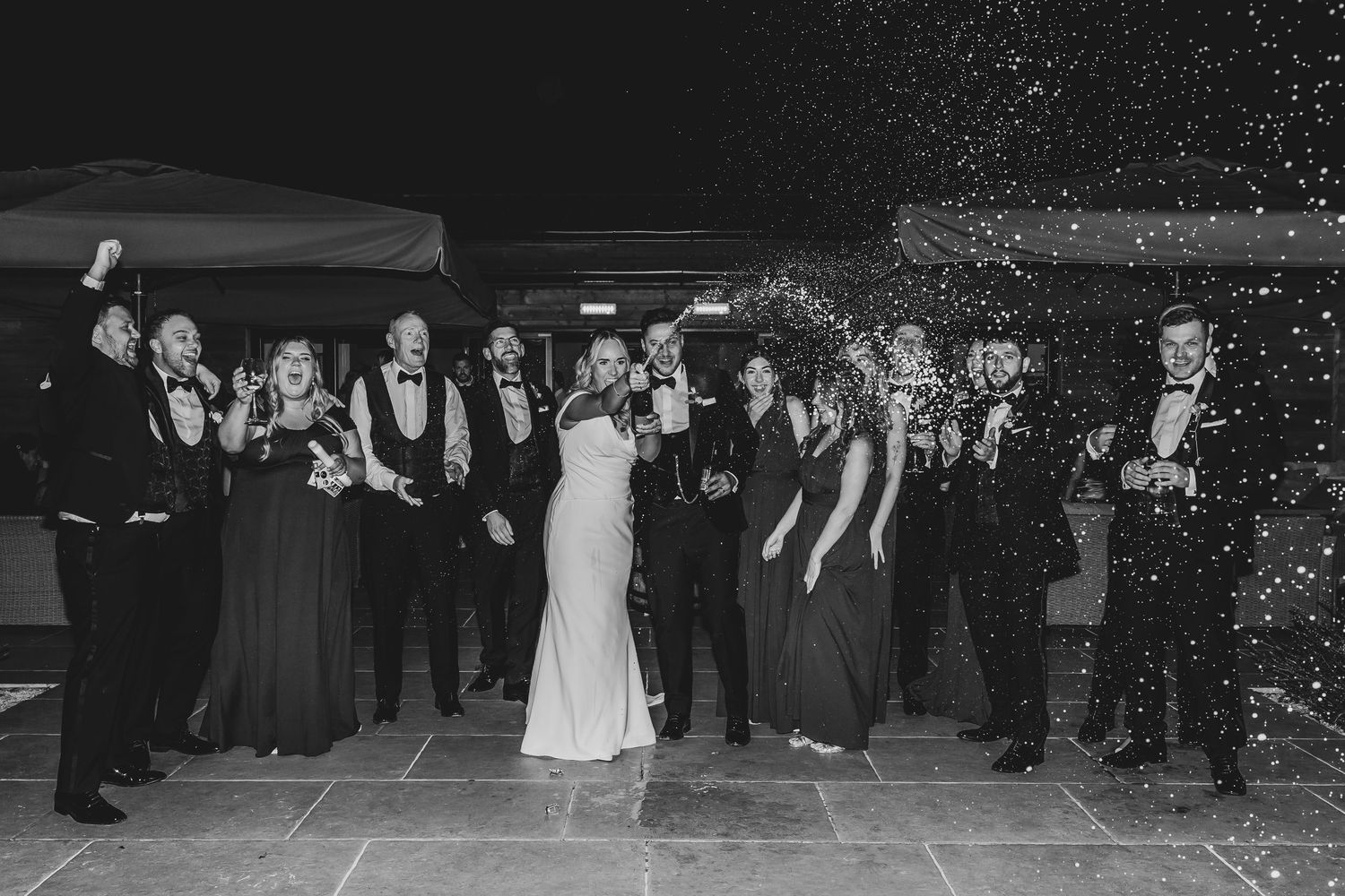 Wedding celebration with guests dancing under twinkling lights at night.