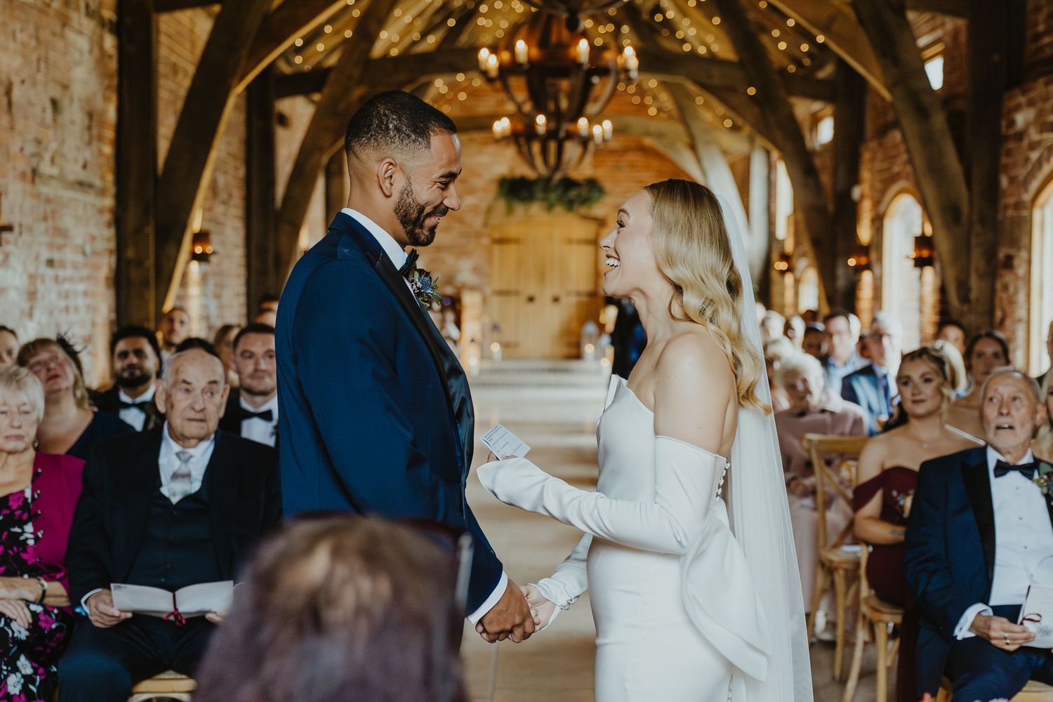 A wedding ceremony takes place in a rustic venue with exposed brick walls and wooden beams overhead.