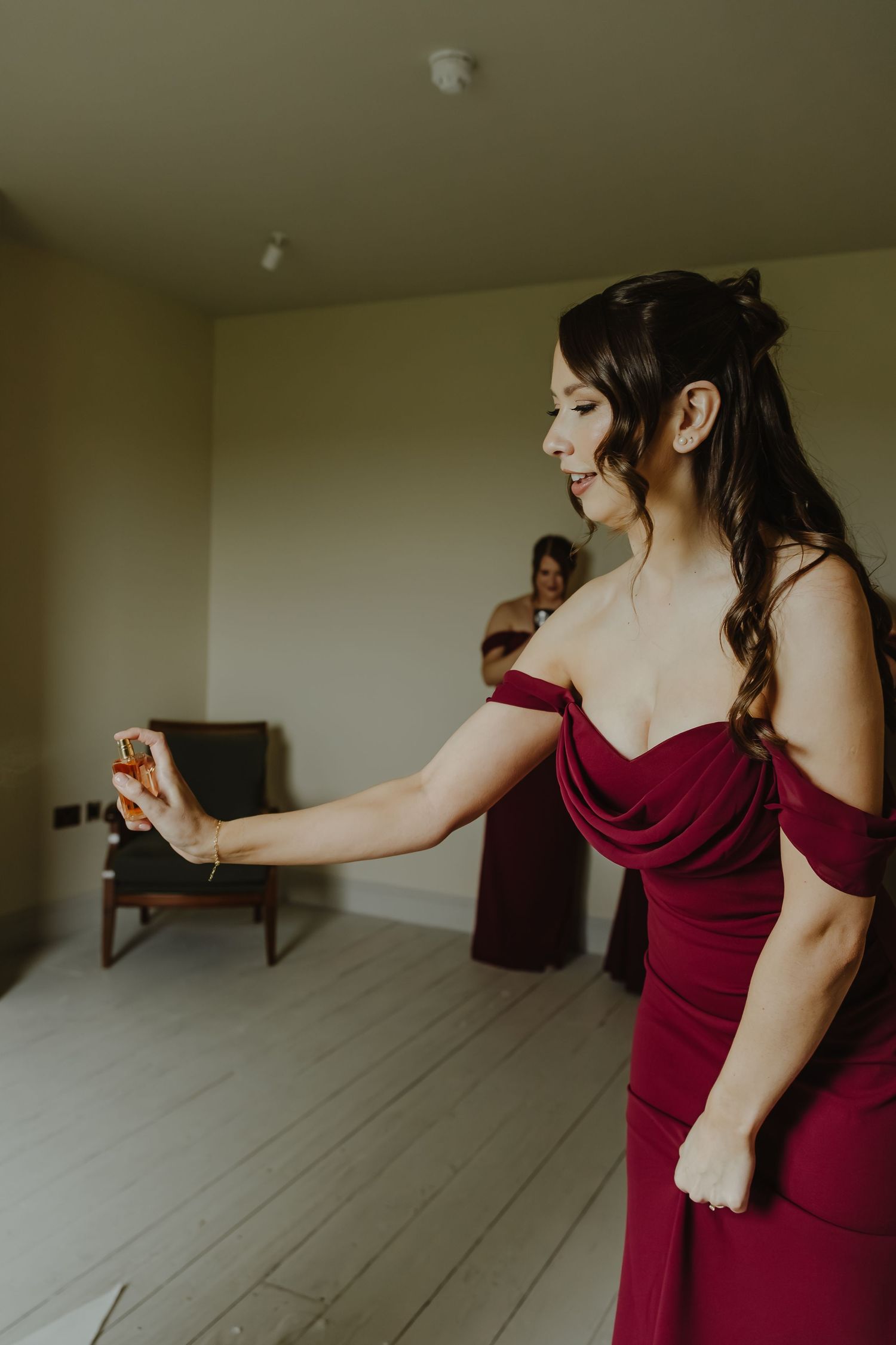 Person in burgundy dress preparing for formal event in minimalist white room.
