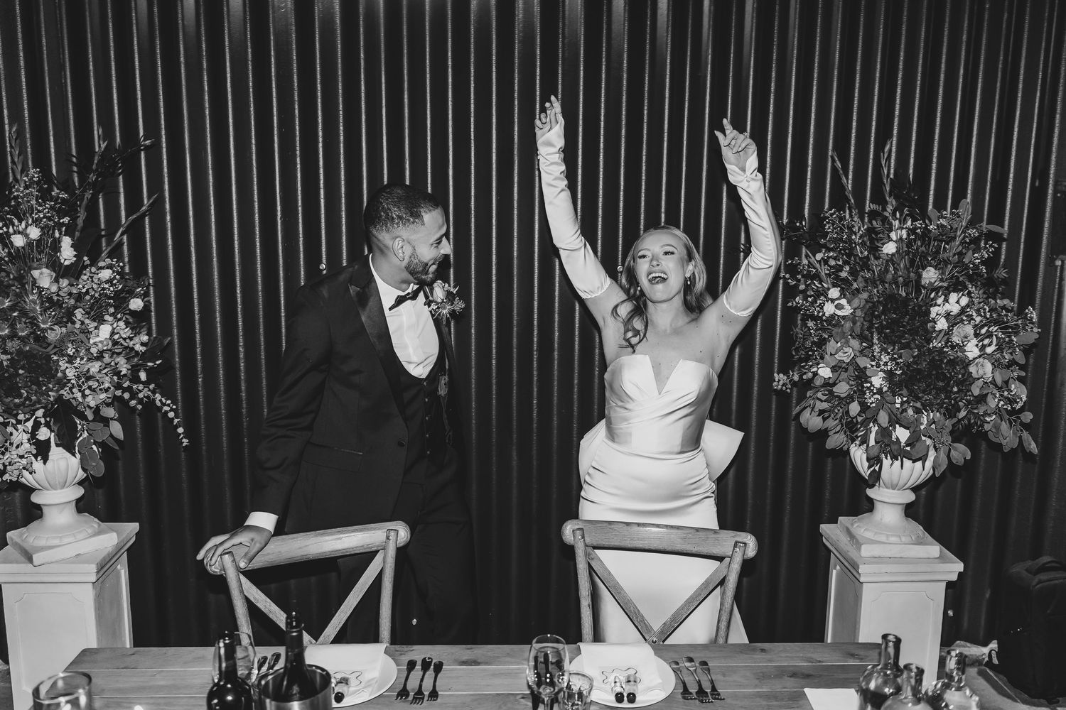 Wedding reception celebration with guests dancing and raising hands against striped backdrop.