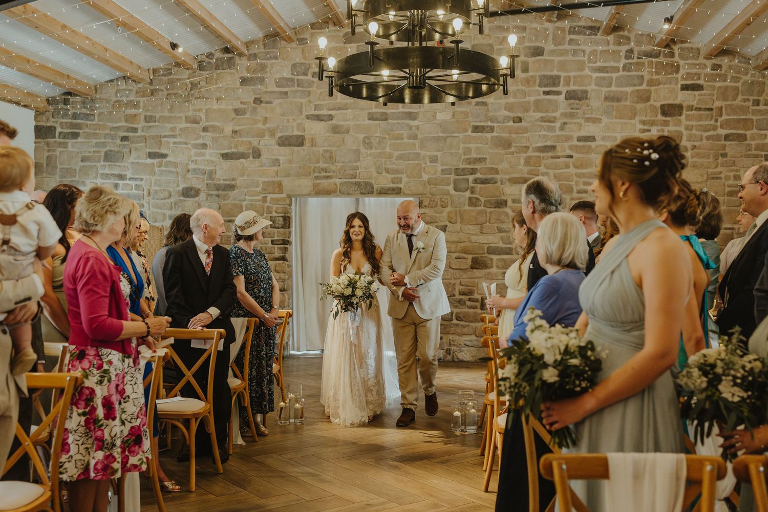 Wedding ceremony in a rustic brick-walled venue with string lights and wooden chairs.