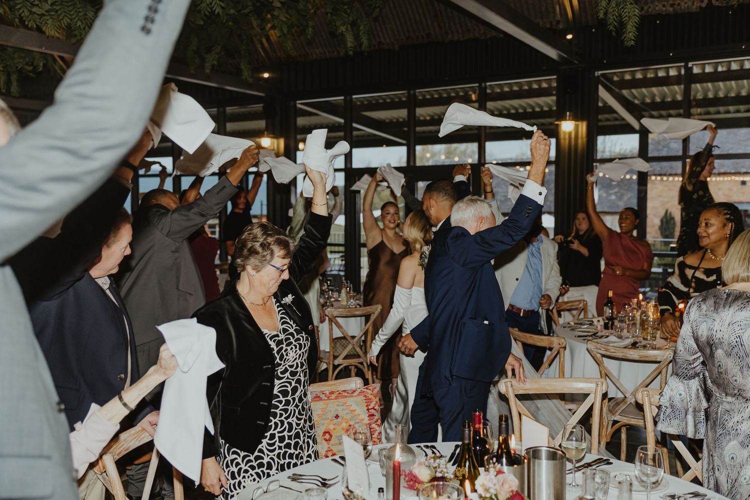 Wedding celebration with guests dancing and mingling in an industrial-style reception space.