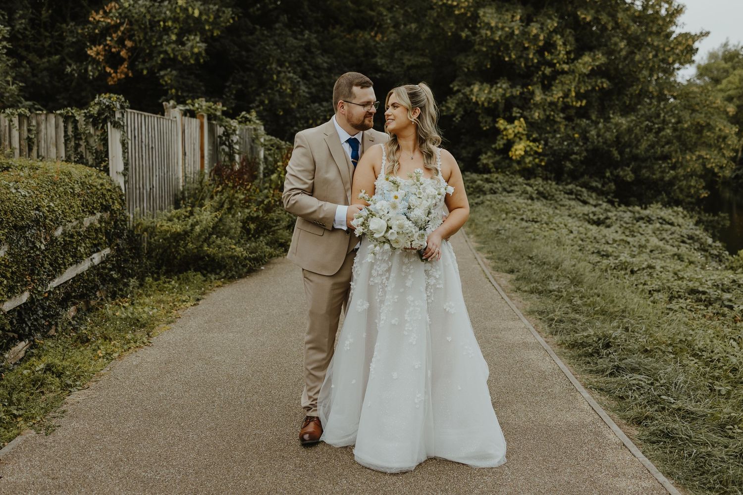 Wedding couple walking along a garden path surrounded by lush greenery.