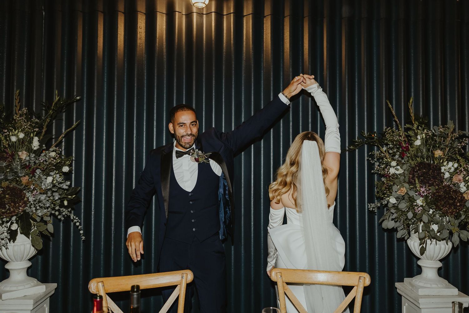 Evening wedding reception with guests celebrating against dramatic black striped wall.