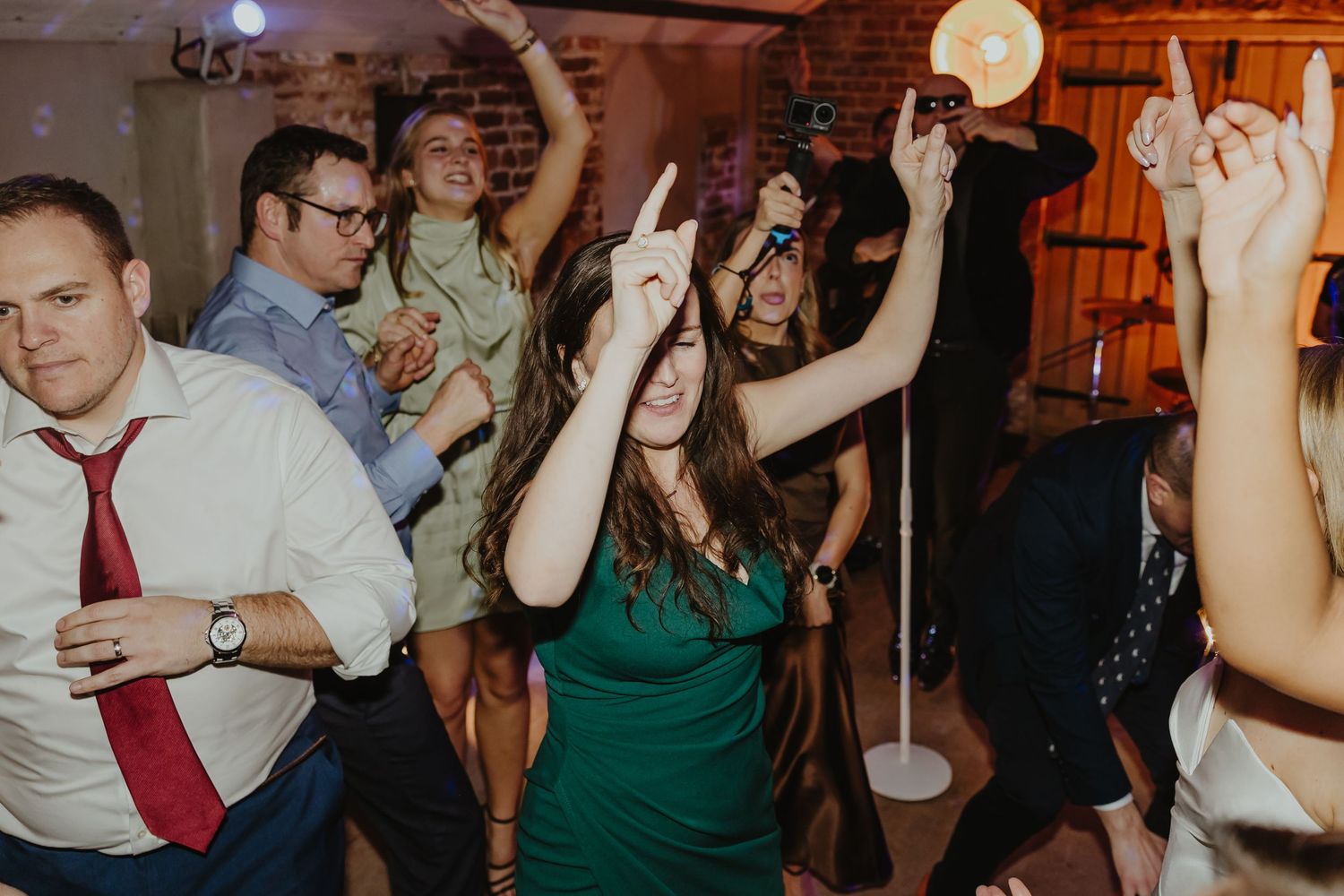 Wedding reception dance party with guests celebrating under warm lighting.
