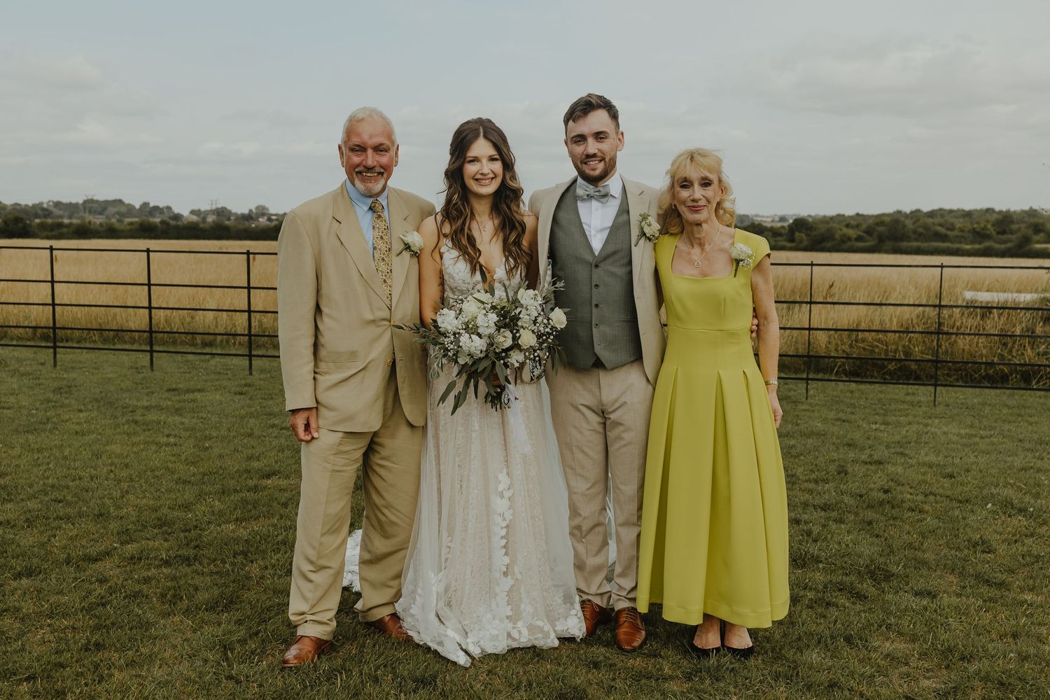 Intimate family wedding photo with couples in formal attire against a countryside backdrop.