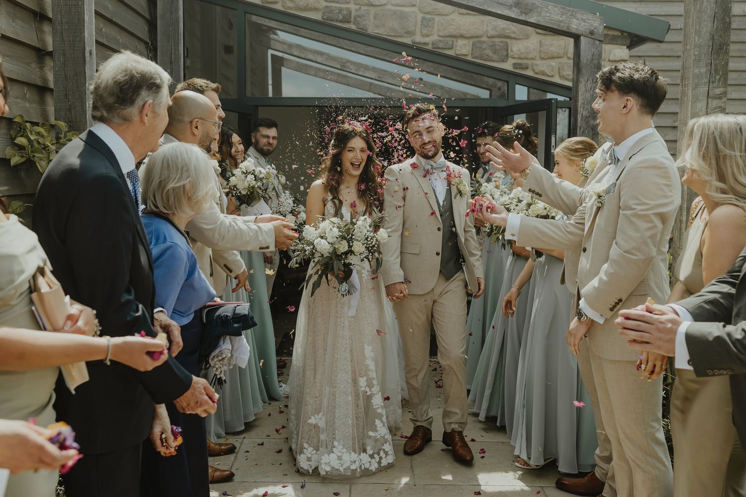 Wedding guests throw flower petals as the newlyweds exit their ceremony.