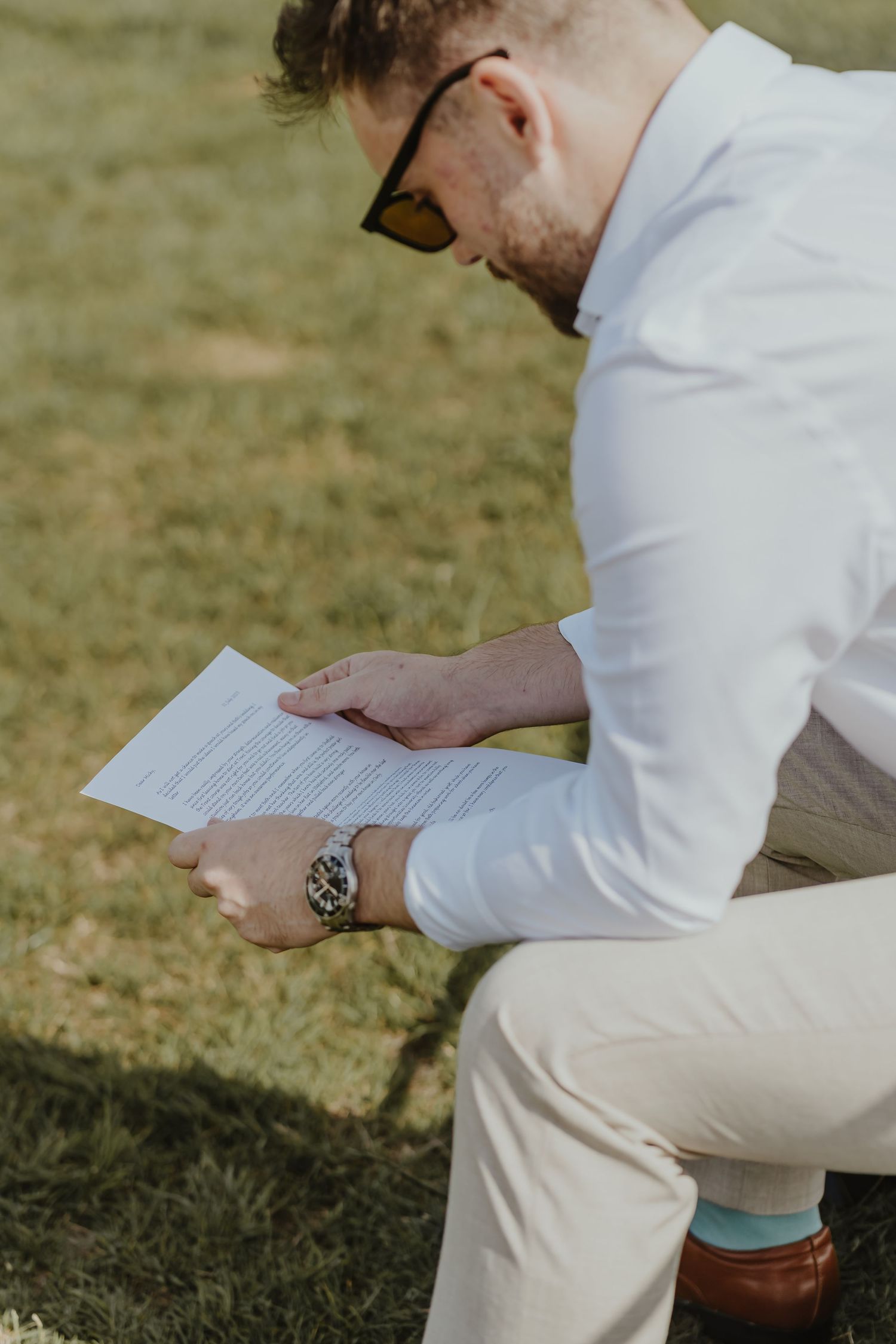 Close-up of someone reading a letter while sitting outdoors wearing a white shirt and beige pants.