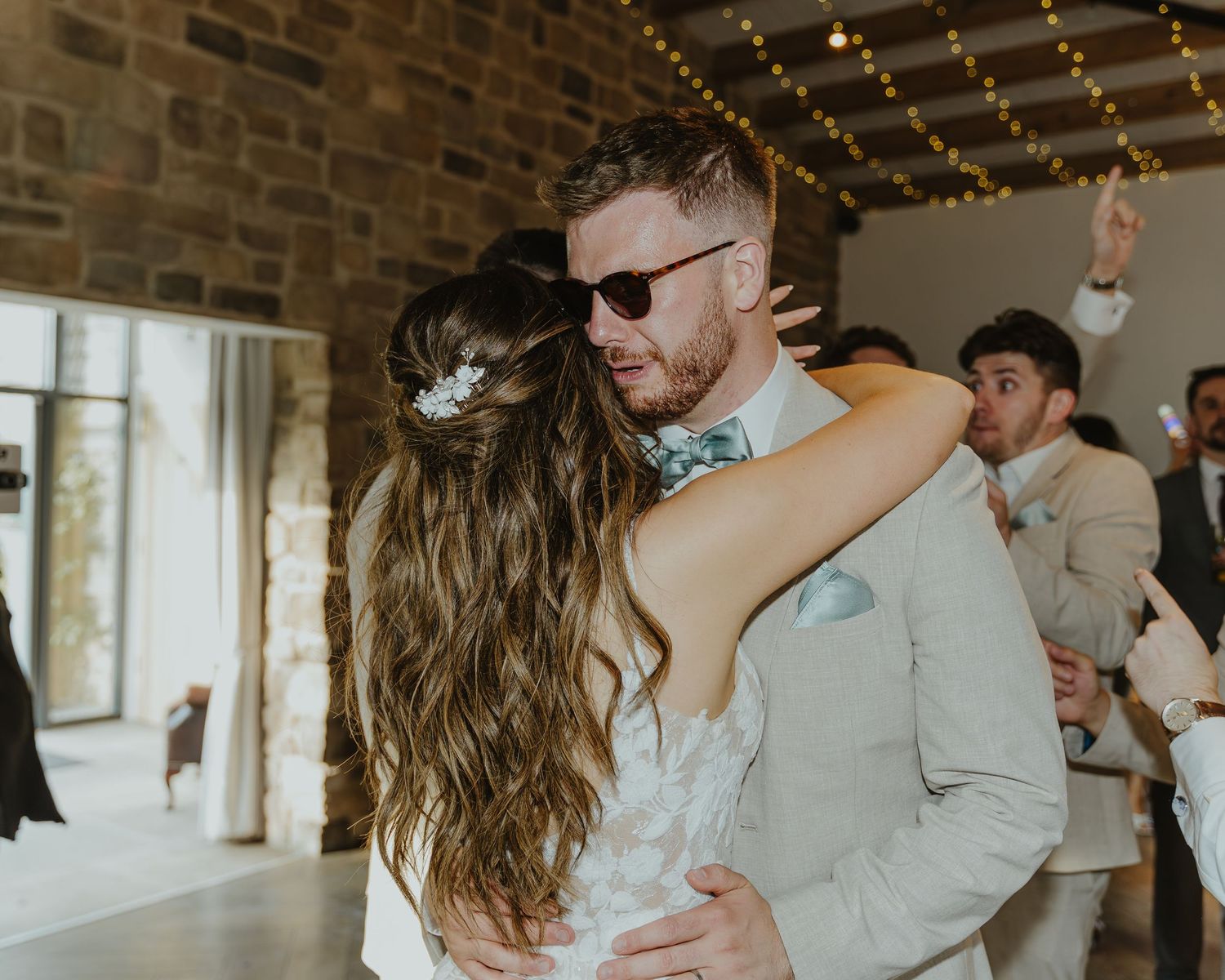 Couples slow dancing at a wedding reception under string lights with exposed brick walls.