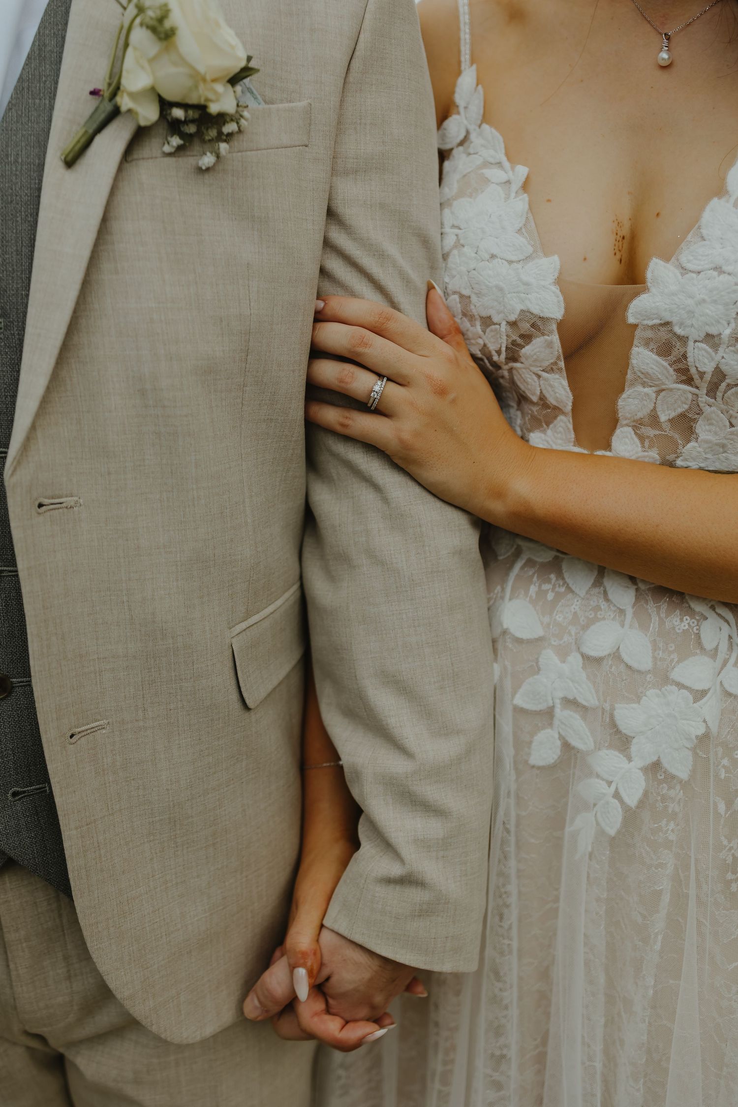 Close-up detail of wedding attire showing a beige suit, floral dress, and rings.