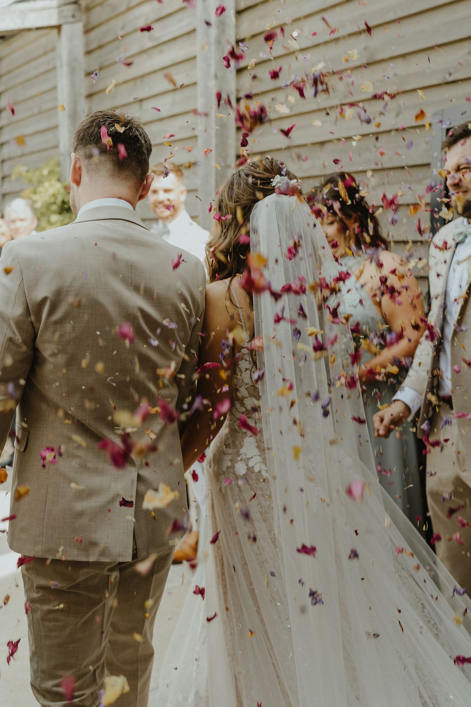 Confetti and flower petals fill the air during outdoor wedding celebration.
