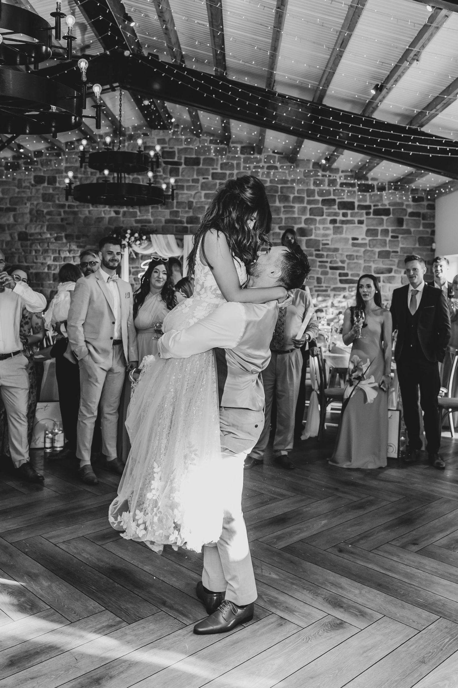 Dramatic wedding dance lift captured in black and white at a rustic brick venue.