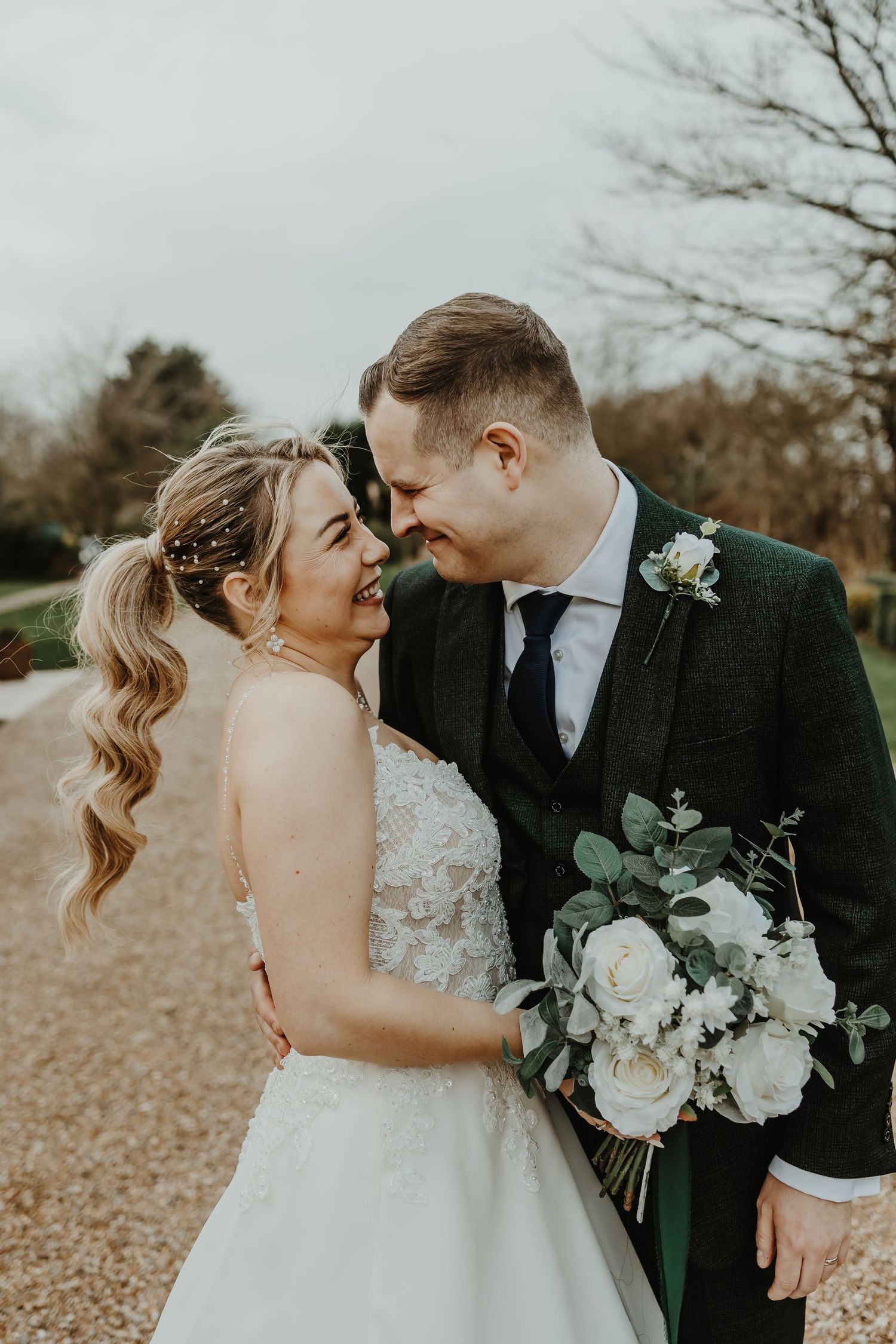 Romantic wedding couple embraces while holding white floral bouquet in outdoor autumn setting.