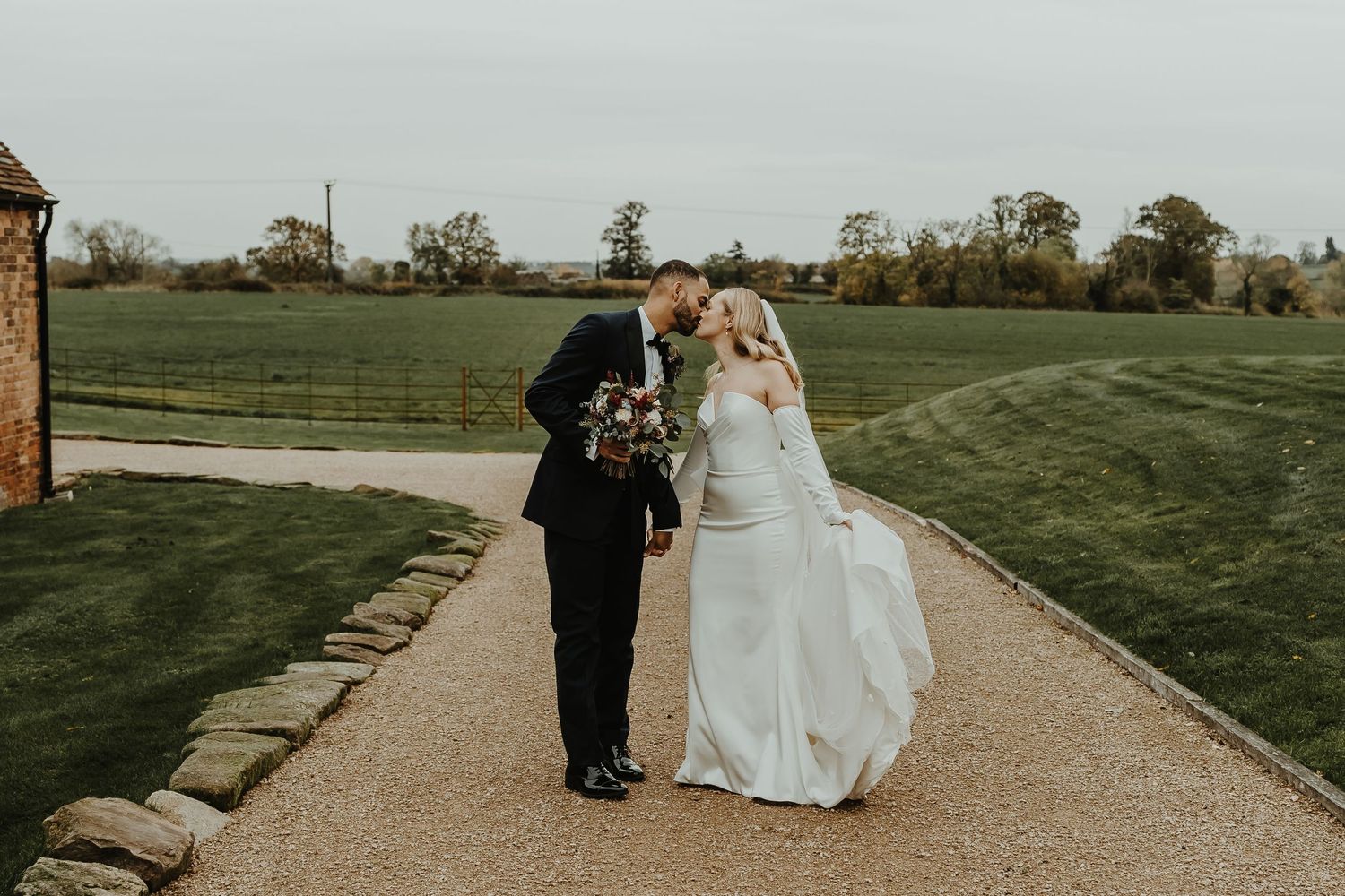 Wedding couple walking along stone pathway surrounded by manicured lawn.