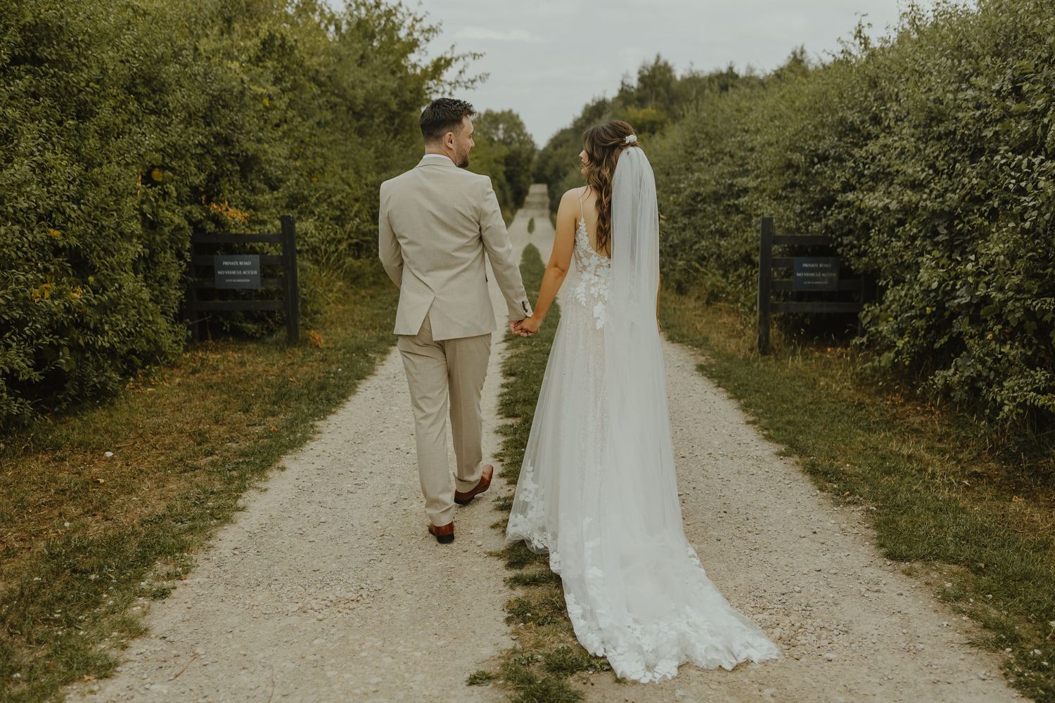 A wedding couple walking hand in hand down a rustic path surrounded by greenery.
