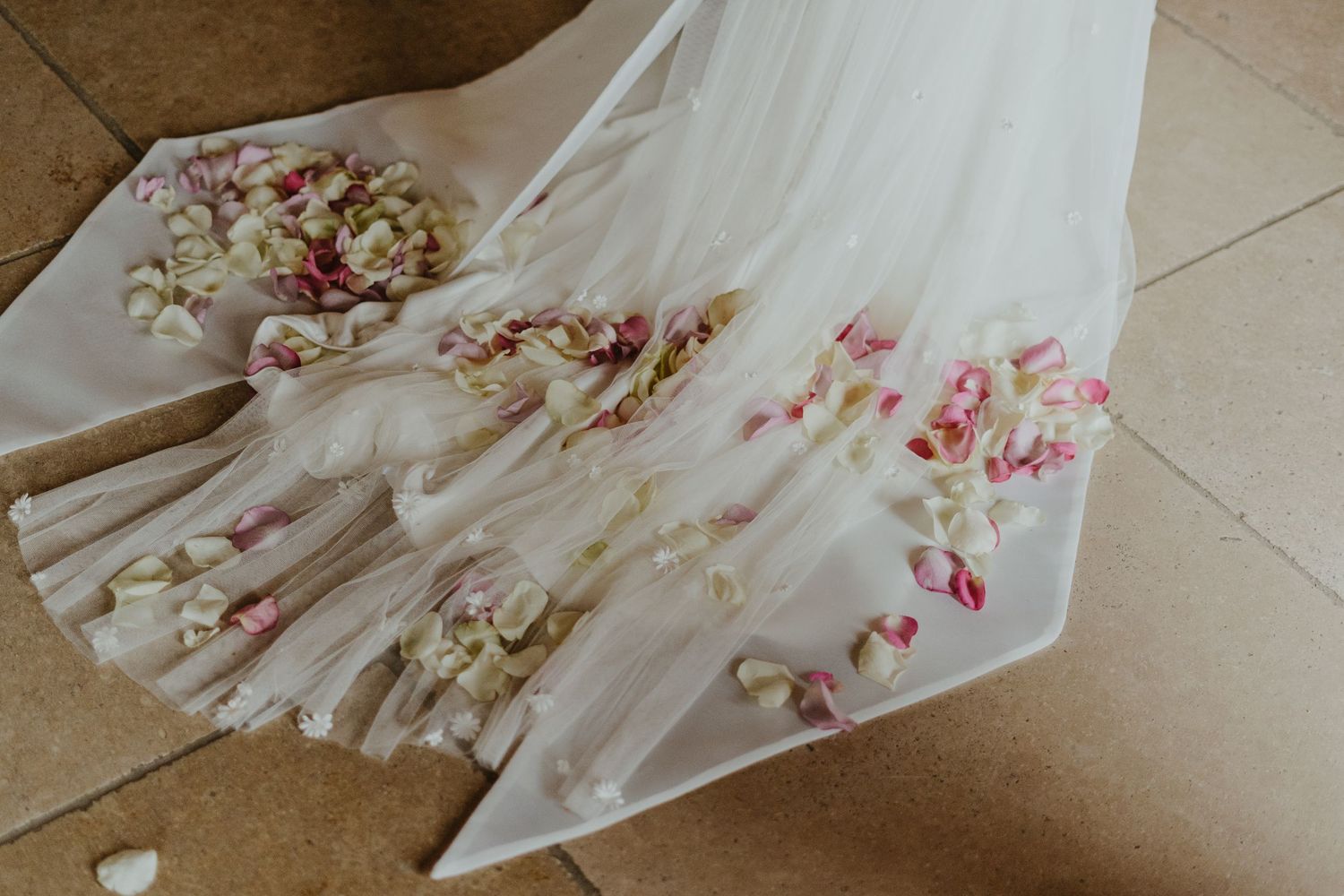 White wedding dress train decorated with scattered rose petals on stone floor.