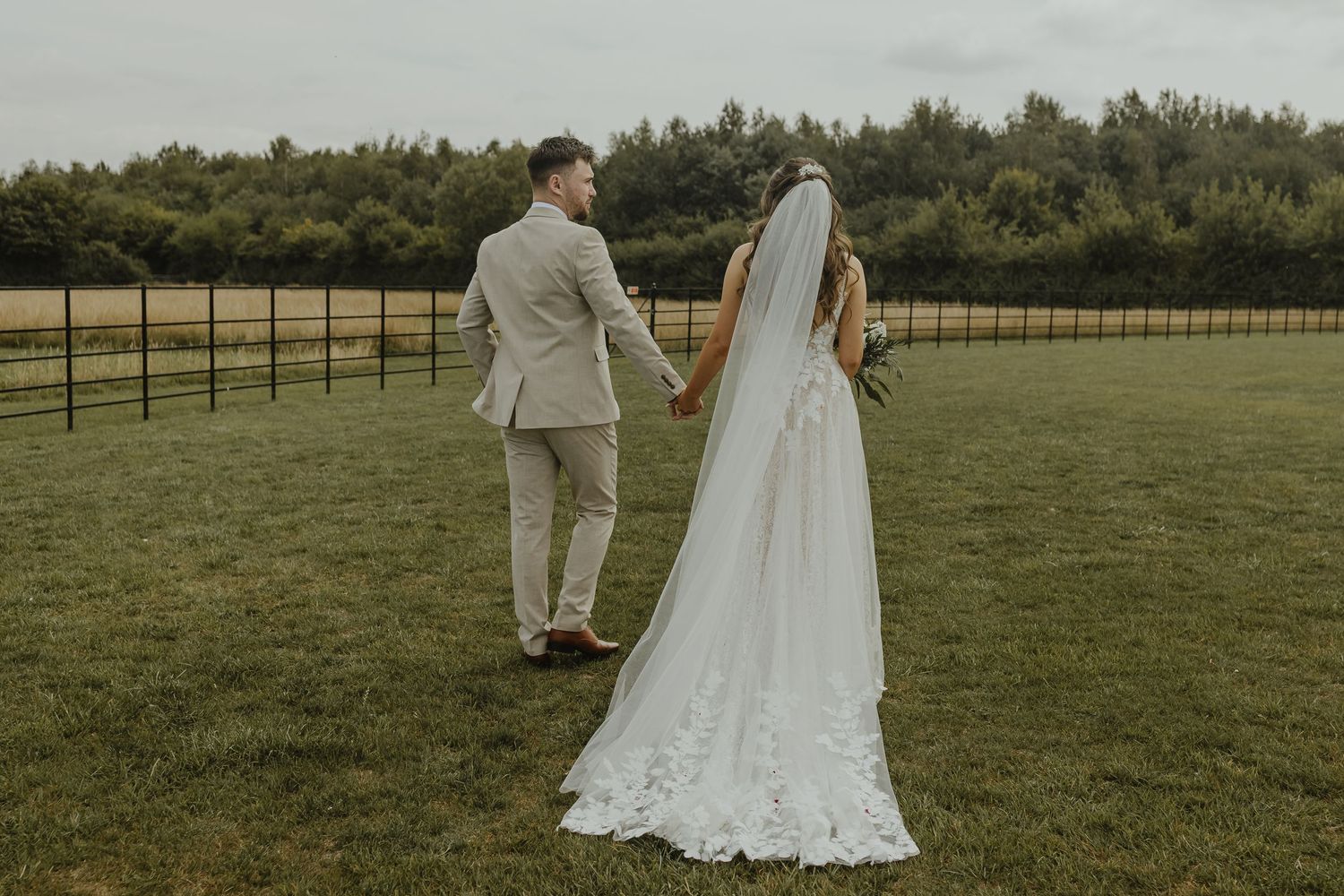 Newlyweds walking hand in hand across a green field on their wedding day.